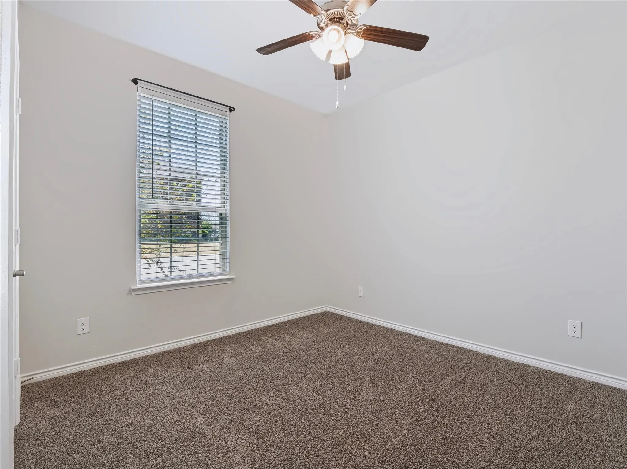 Carpeted flooring, neutral wall tones, window with horizontal blinds, and a ceiling fan with integrated lighting
