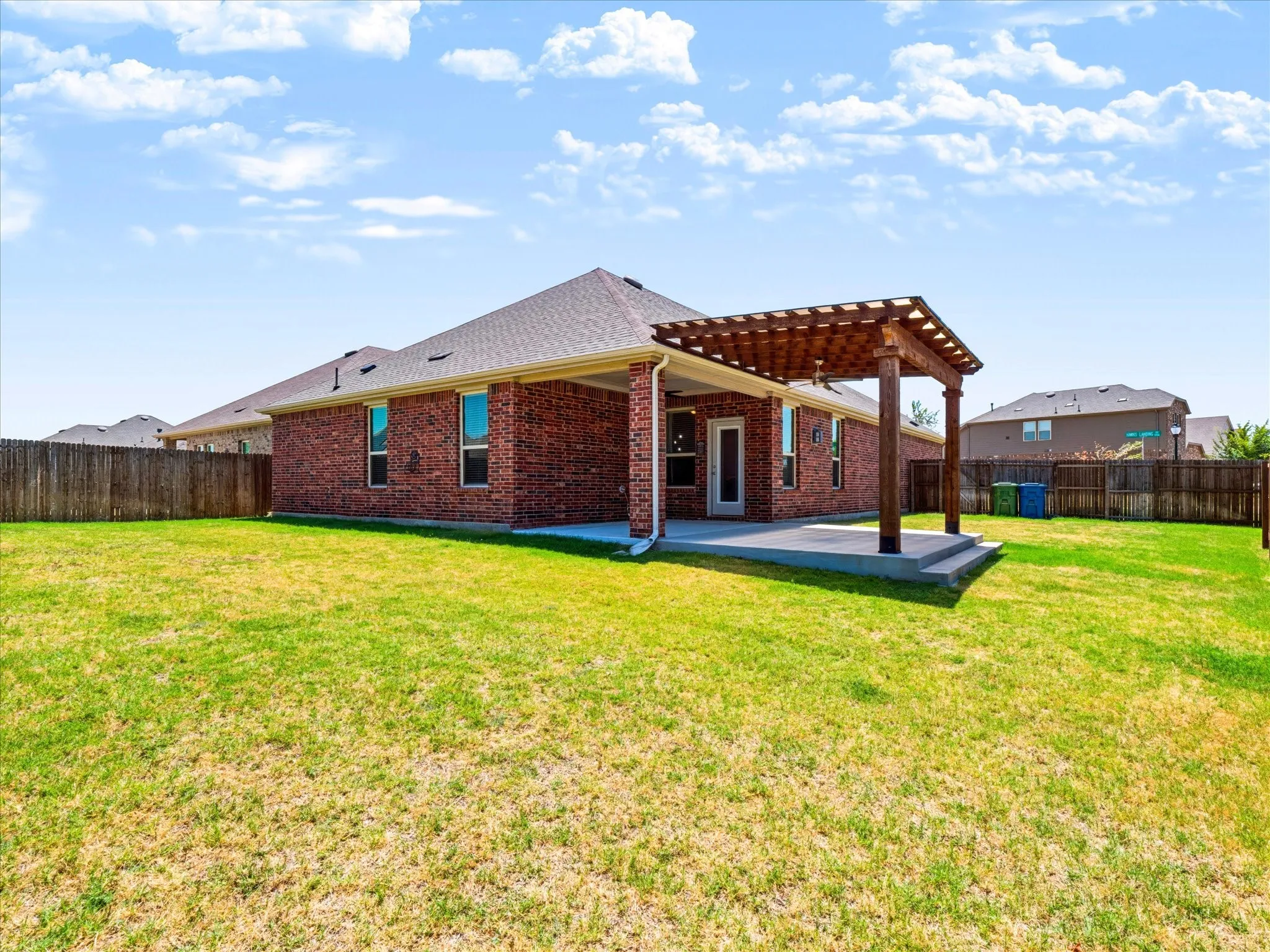Brick exterior with a covered patio, a wooden pergola, and a fenced backyard