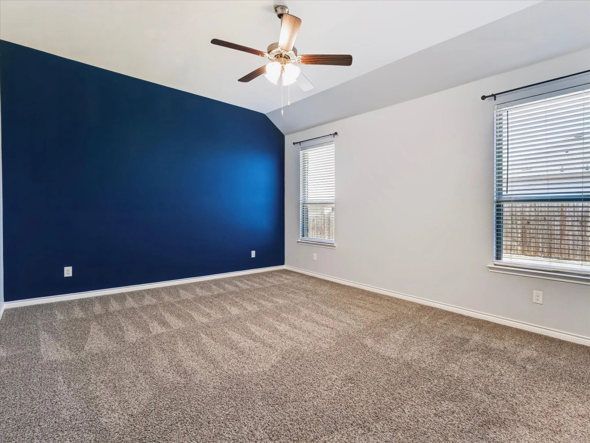Spacious interior with plush carpet flooring, multiple windows, a ceiling fan fixture, and a distinctive accent wall