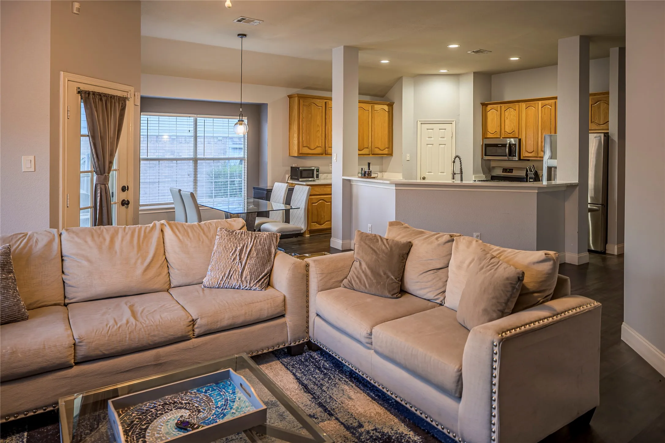 Open-concept living area featuring dark wood-finish flooring, recessed lighting, and a kitchen with wood cabinetry and stainless steel appliances