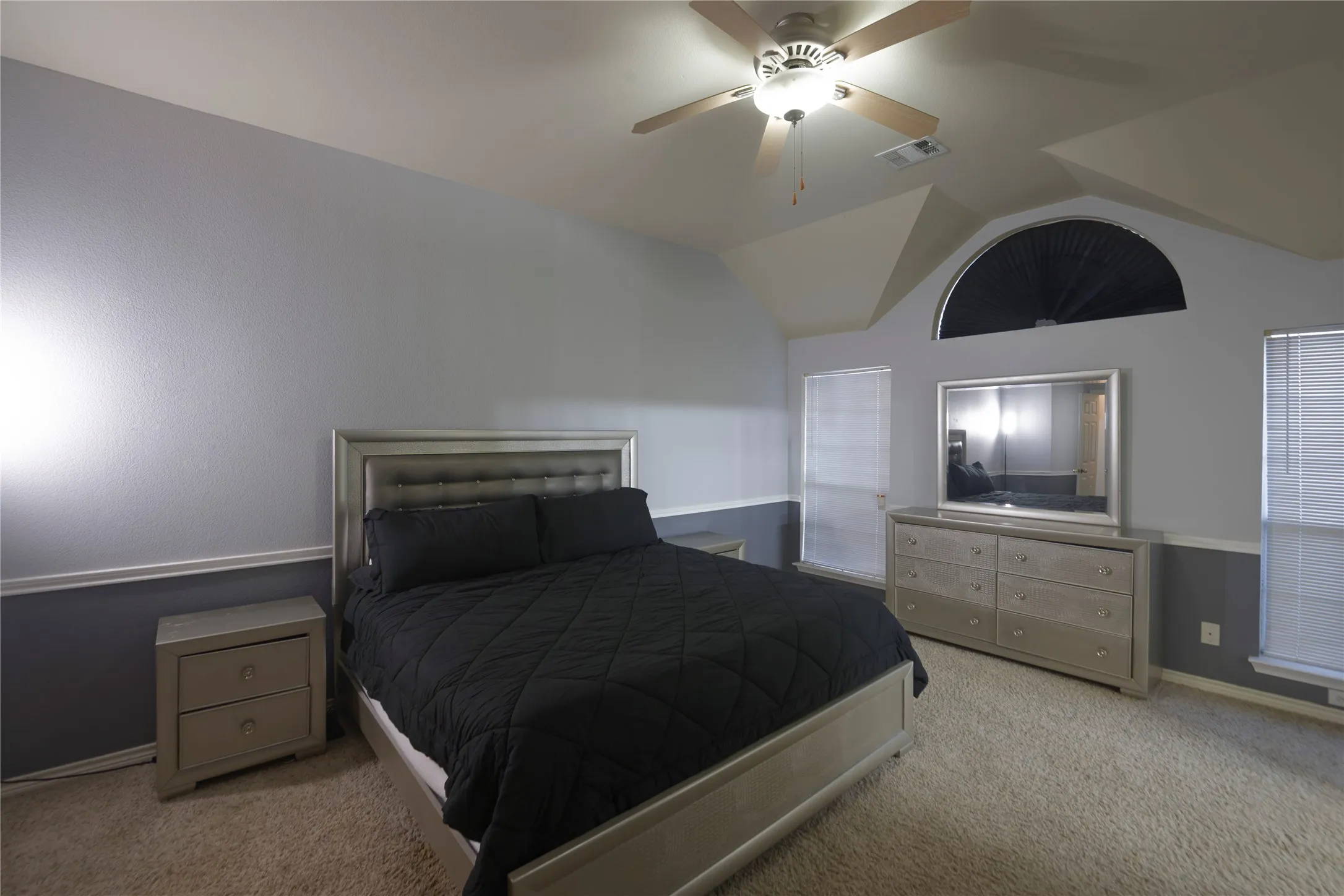 Vaulted ceiling with ceiling fan, arched window, and carpeted flooring