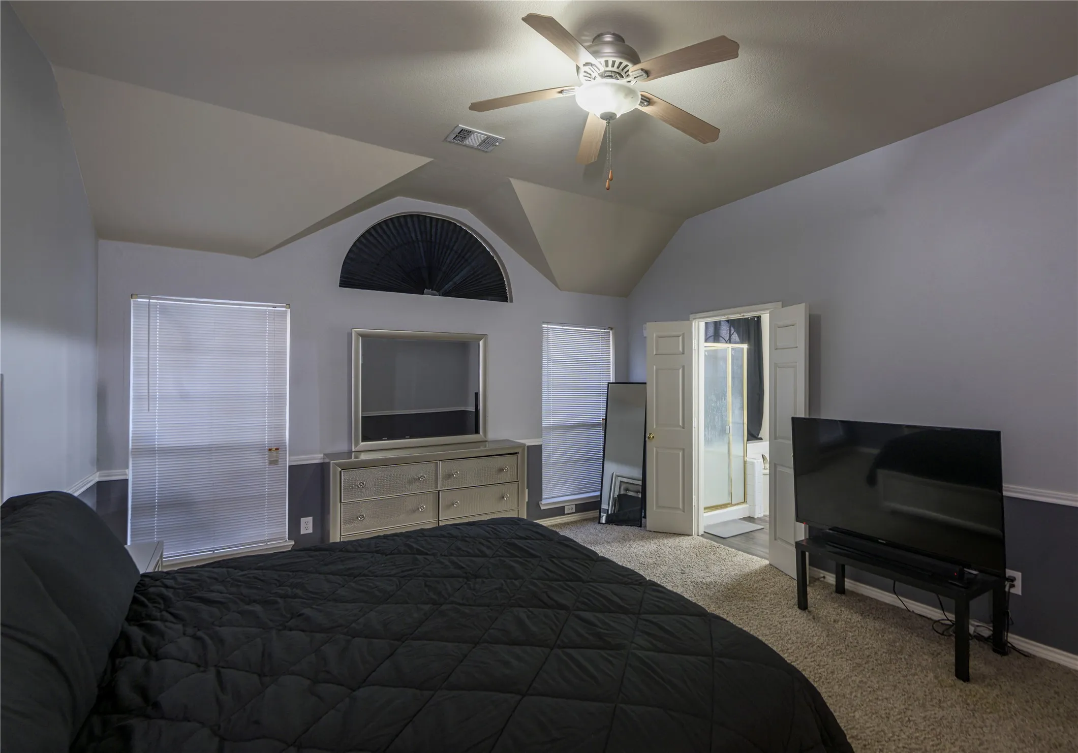 Vaulted ceiling, ceiling fan with light fixture, arched window with blinds, two windows with blinds, carpeted flooring