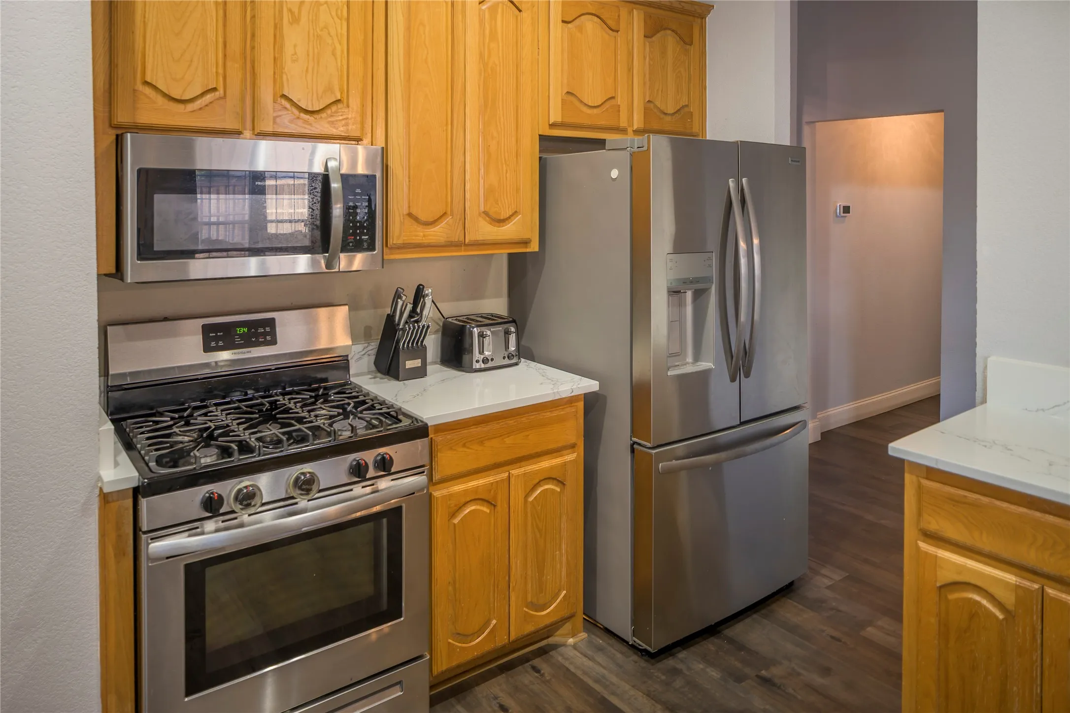 Stainless steel appliances, wood cabinetry, light-toned countertops, and wood-finish flooring