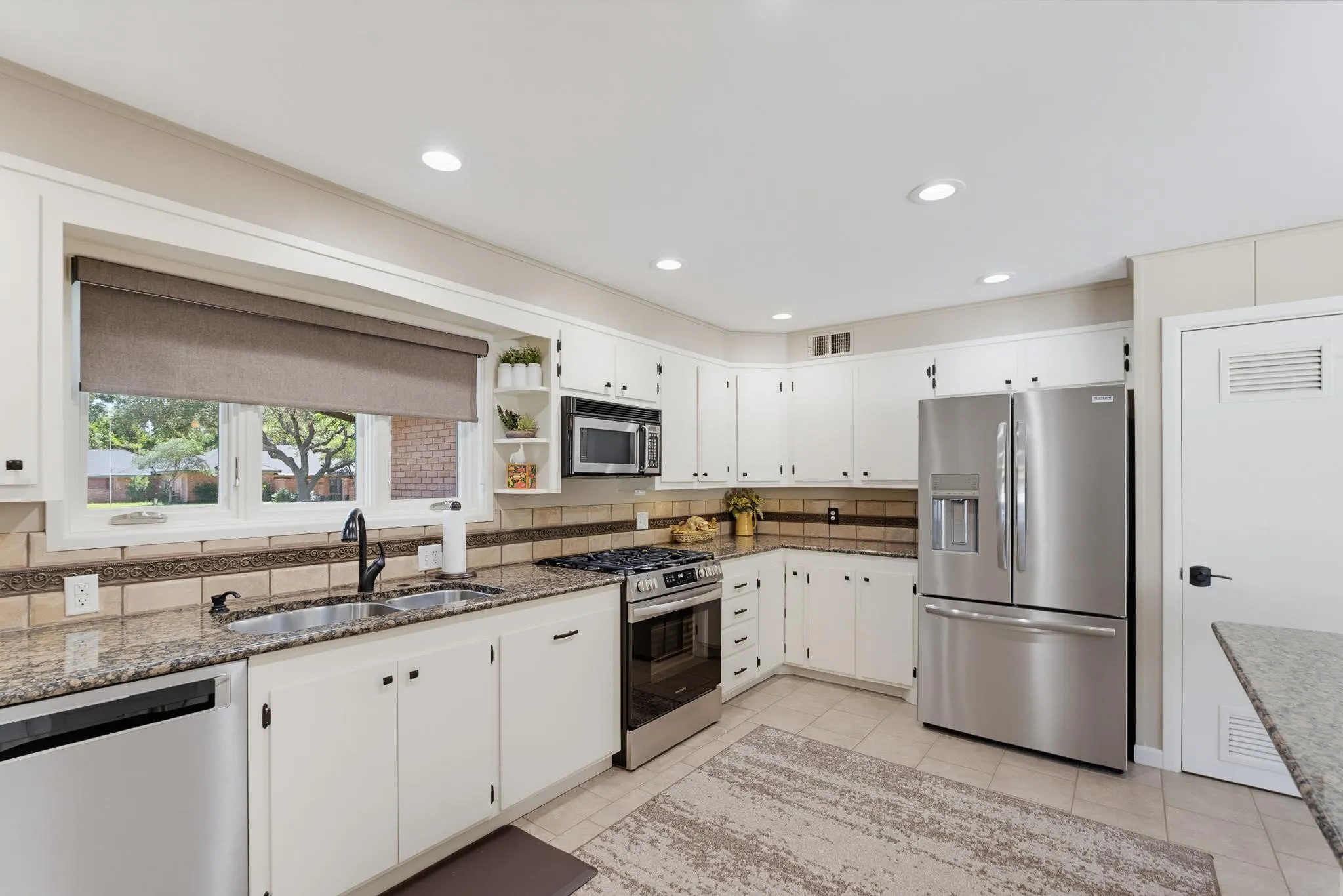 White cabinetry, stainless steel appliances, granite countertops, tile backsplash, and recessed lighting