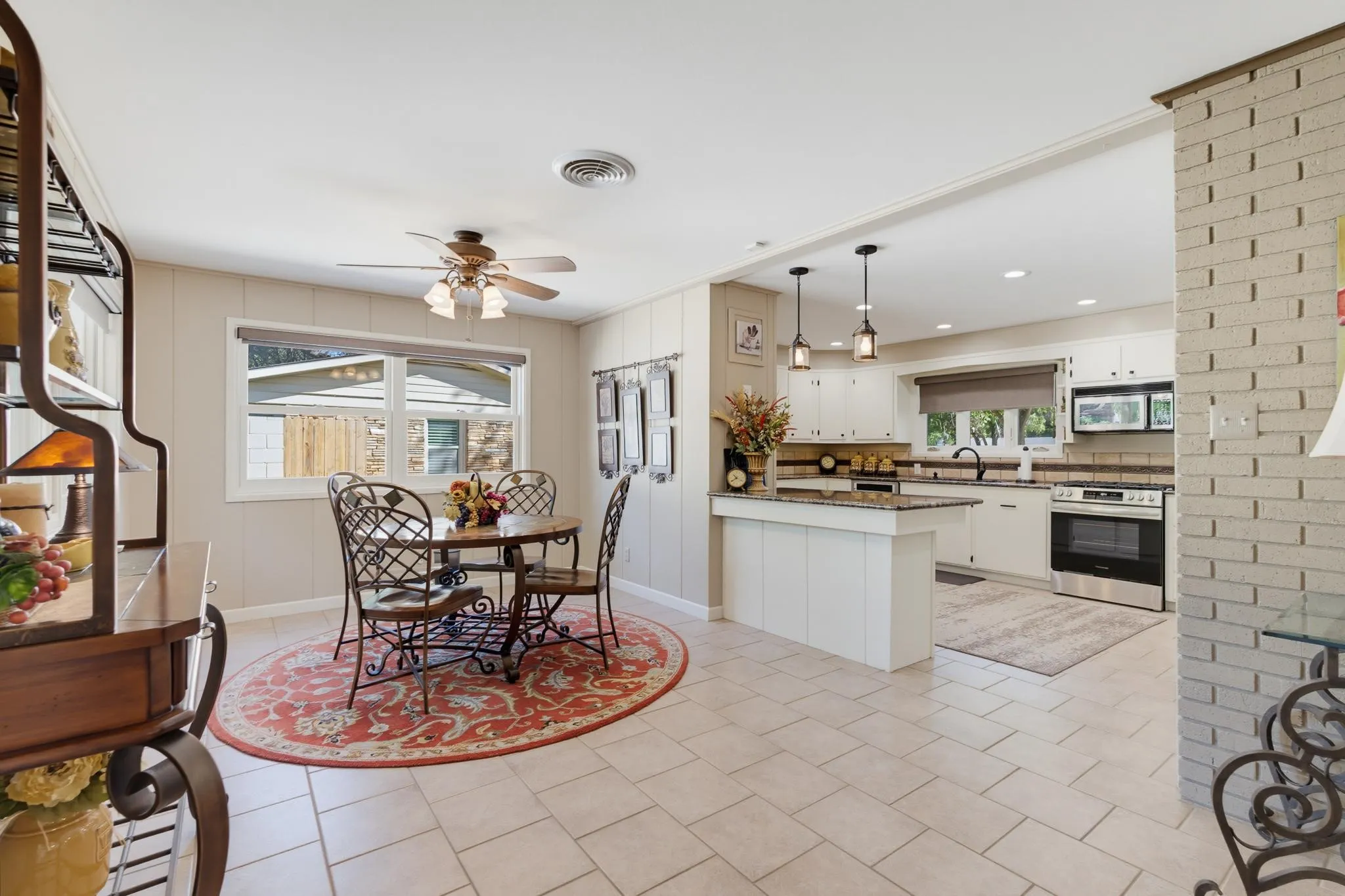 Open-concept living space with tile flooring, white kitchen cabinetry, stainless steel appliances, and a kitchen island with pendant lighting