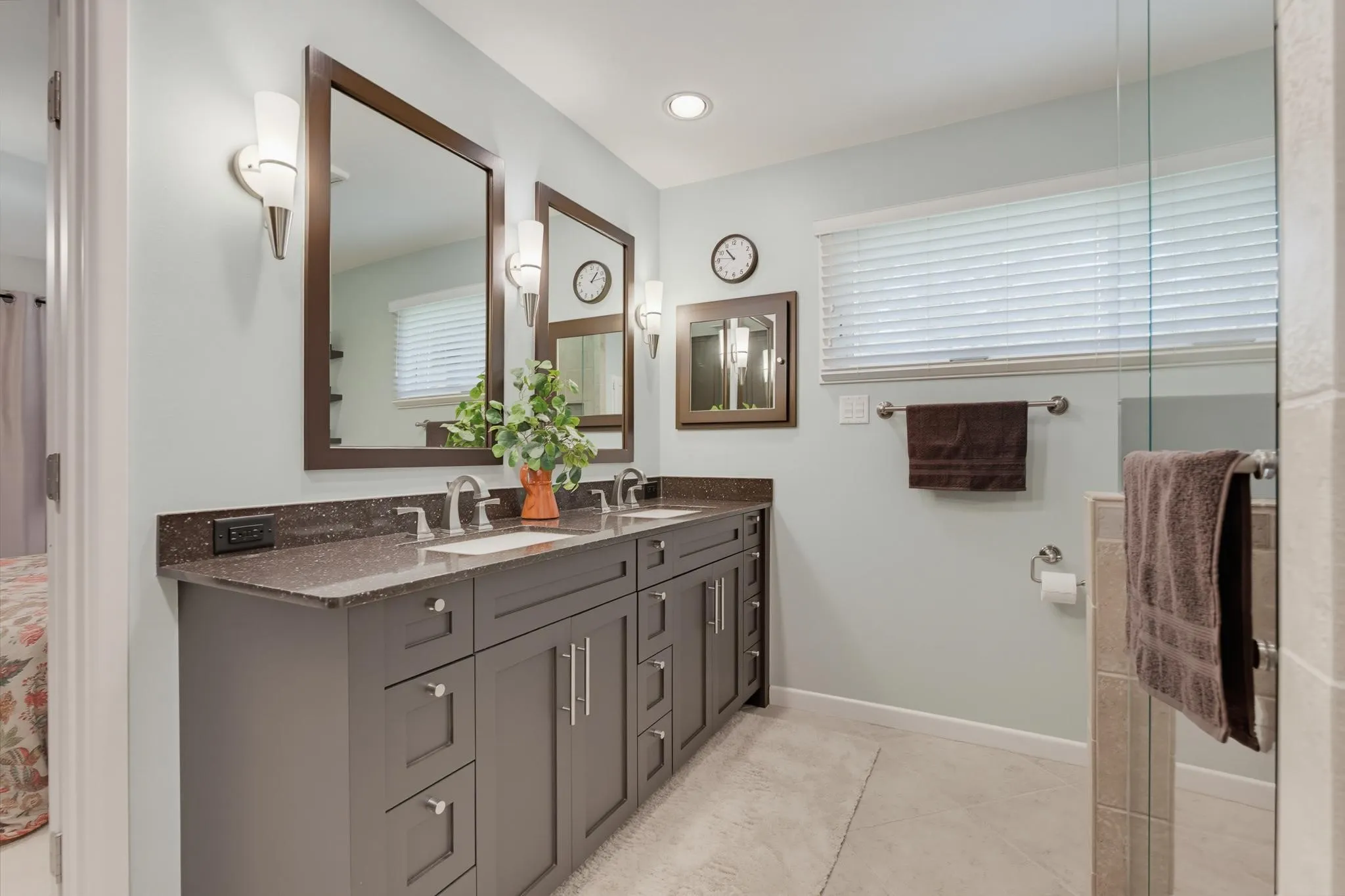 Dual vanity with dark wood-finish framed mirrors, sconce lighting, stone-finish countertop, and undermount sinks