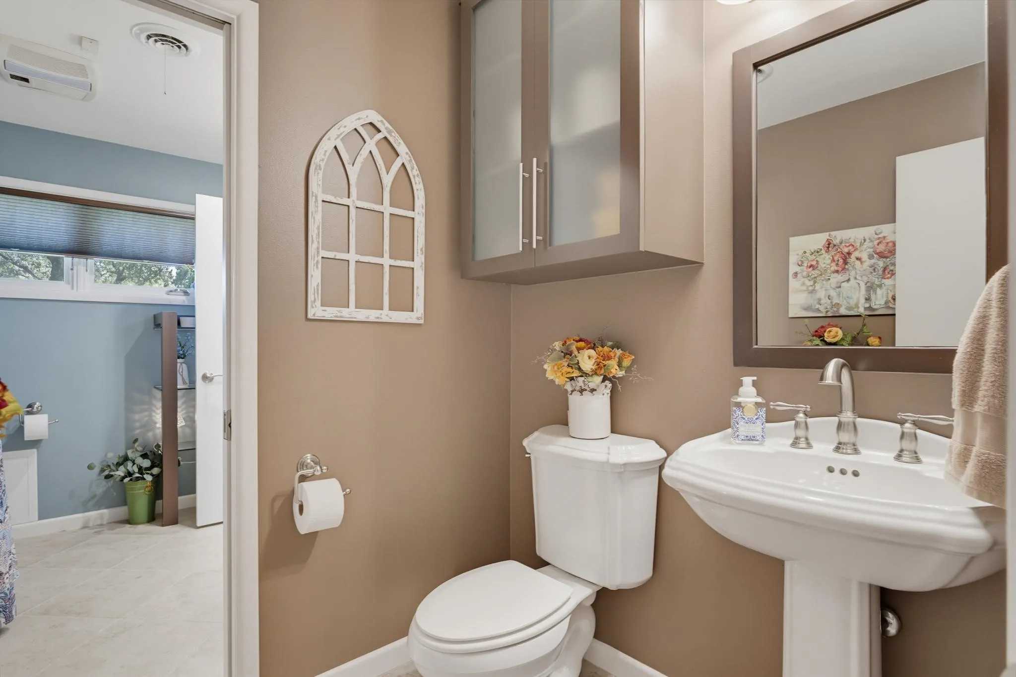 Pedestal sink with polished chrome fixtures, framed mirror, and upper cabinetry with frosted glass inserts