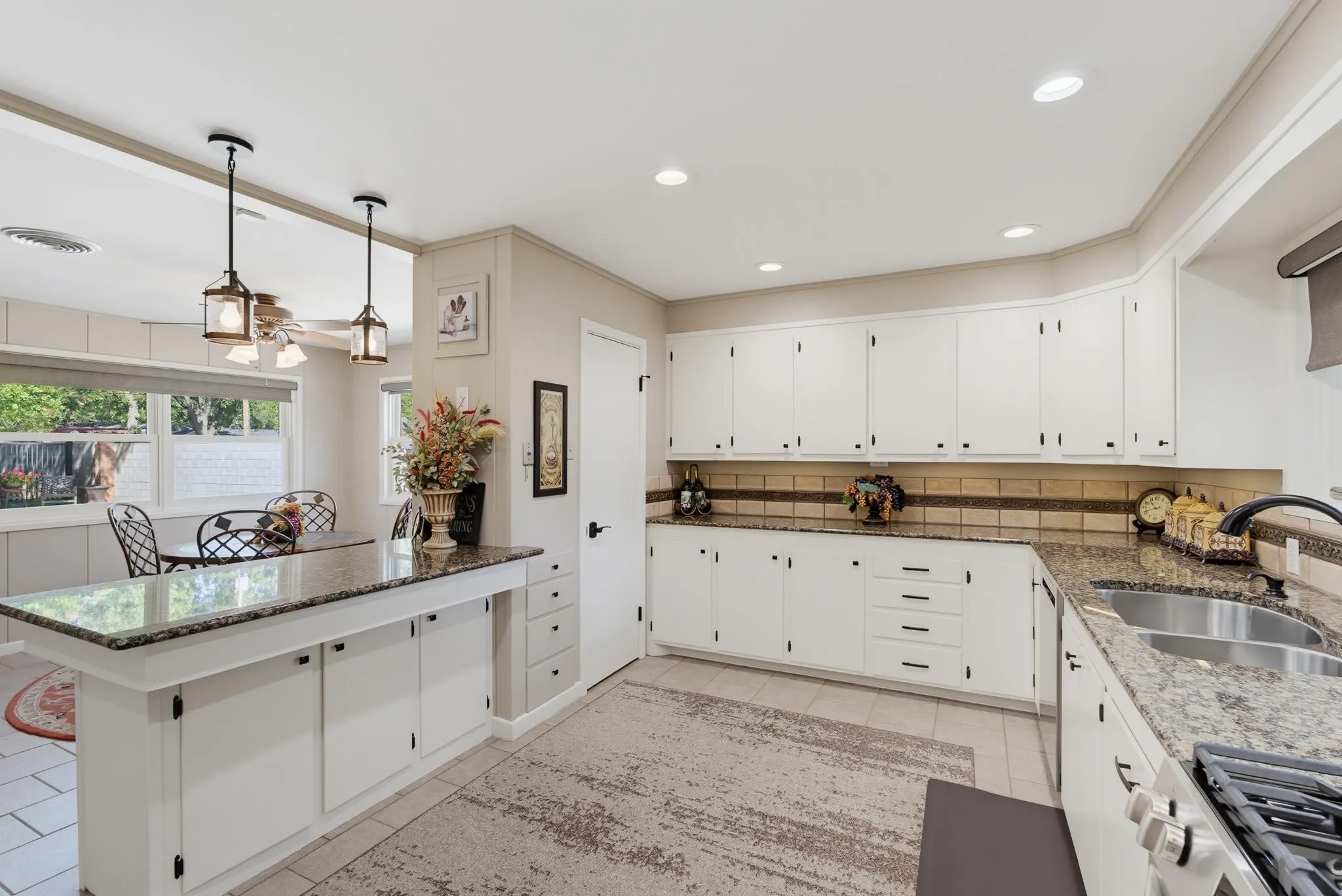 White cabinetry with dark hardware, granite-style countertops, stainless steel double basin sink, and recessed lighting