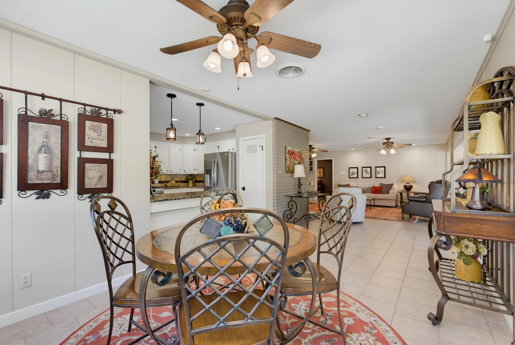 Open-concept layout featuring tile flooring, ceiling fans, and an adjacent kitchen with pendant lighting