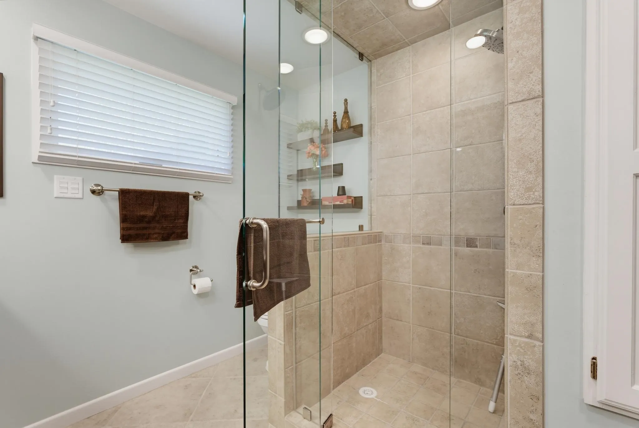 Glass-enclosed shower with full-height tile surround, recessed lighting, and integrated wall shelving
