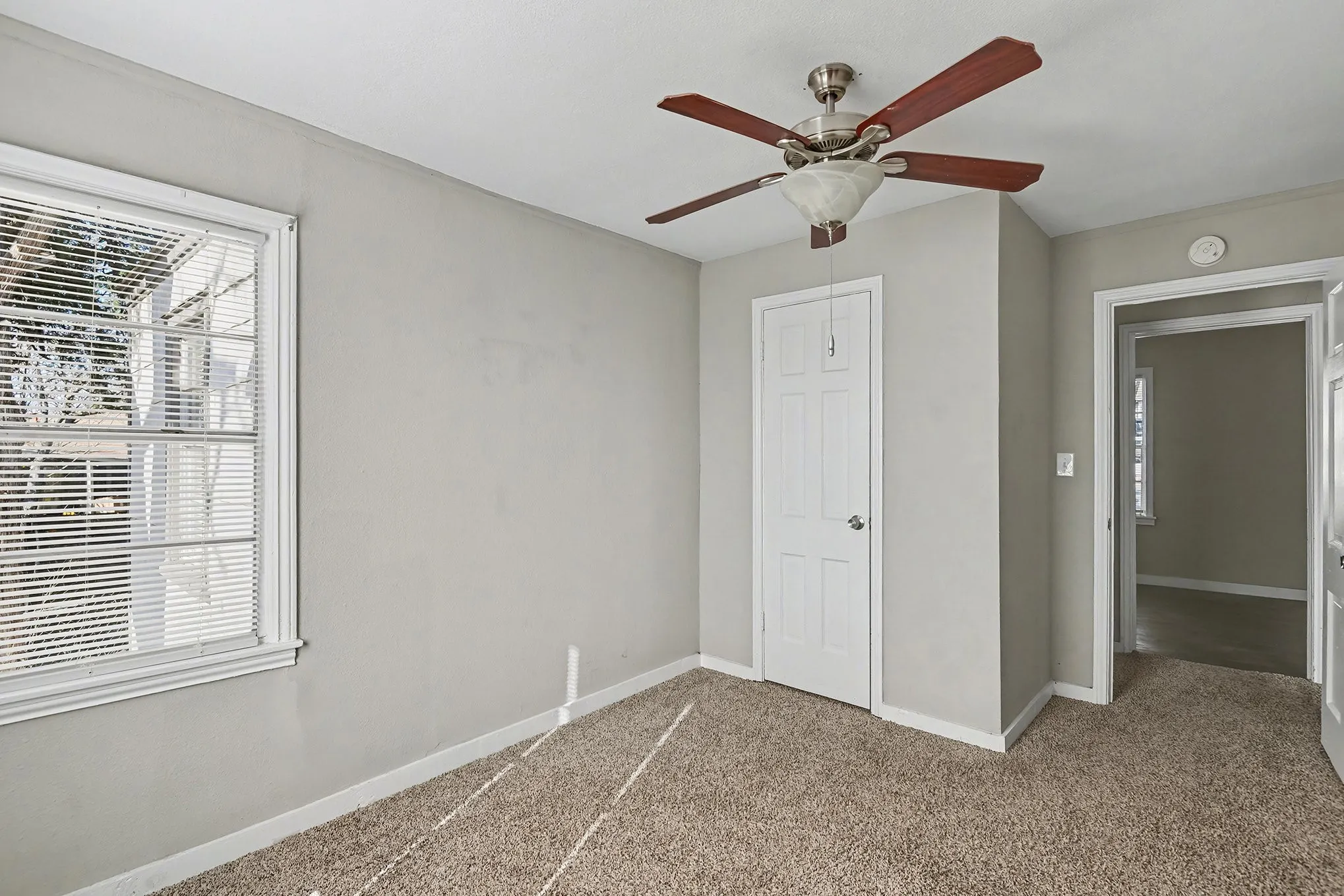 Neutral wall finishes, textured carpeting, ceiling fan with integrated lighting, paneled interior door, and window with blinds