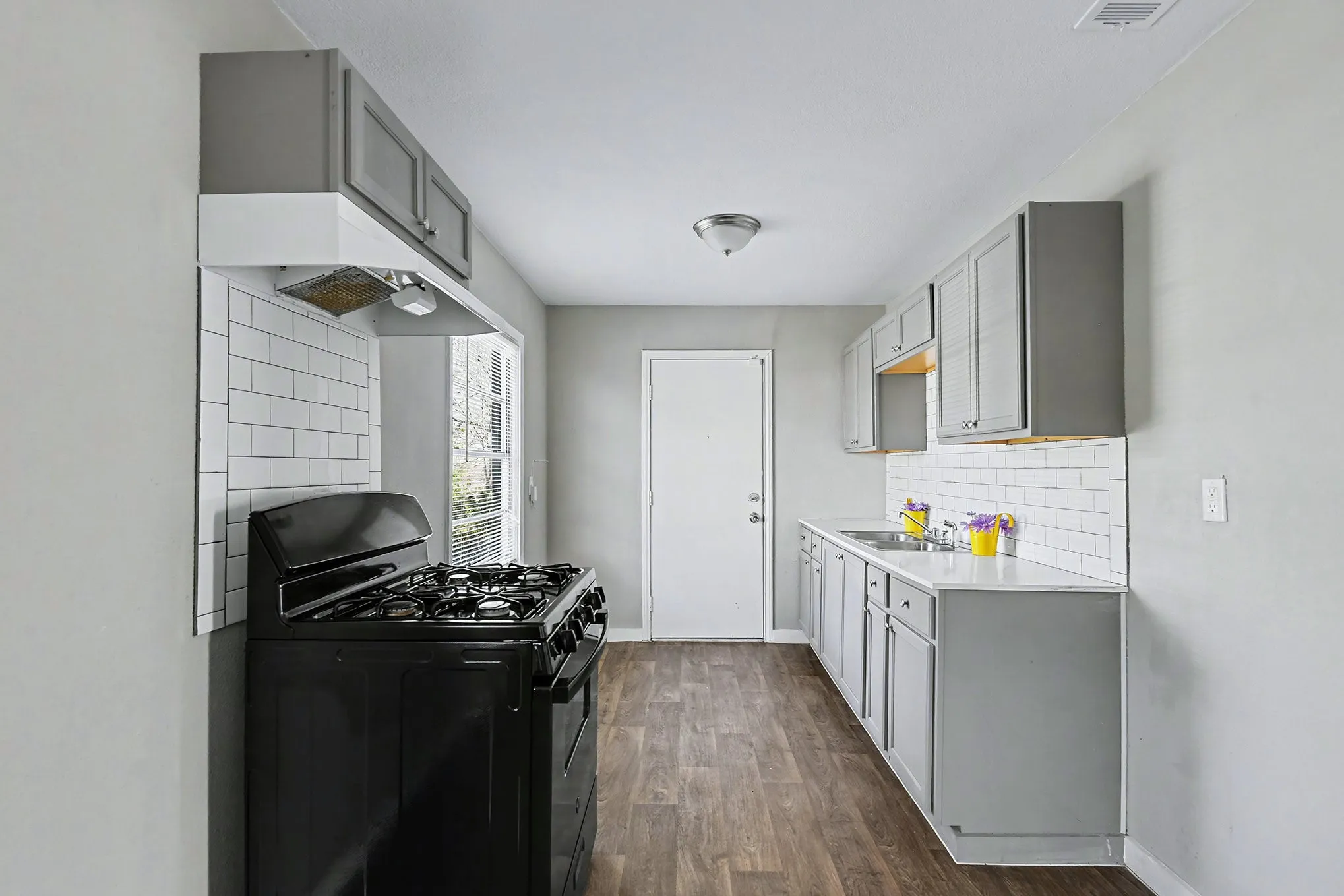 Kitchen featuring grey cabinetry, white countertops, white subway tile backsplash, wood-finish flooring, and a built-in range hood