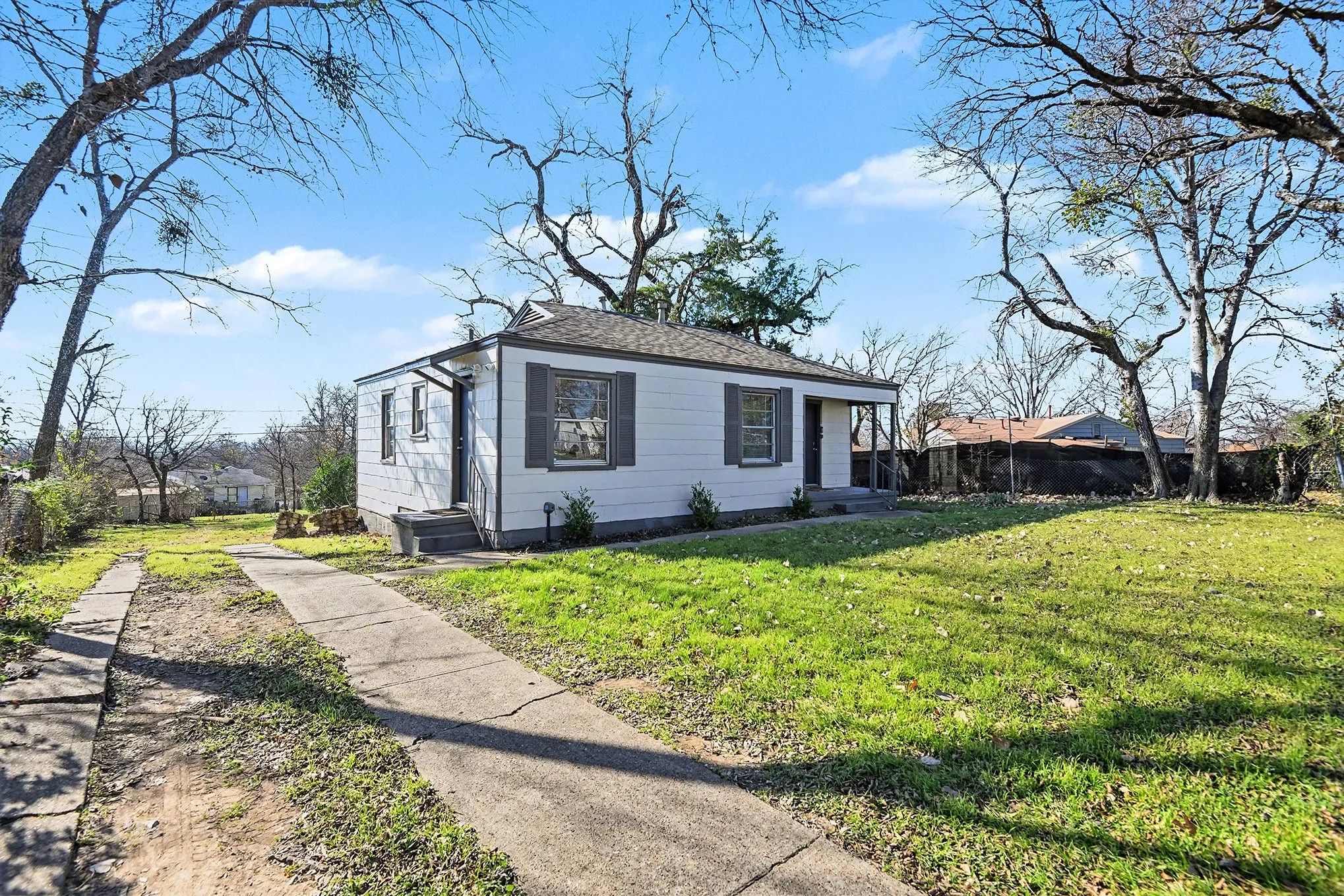 White exterior siding, gray window shutters, covered porch entry, concrete driveway, and a spacious front lawn