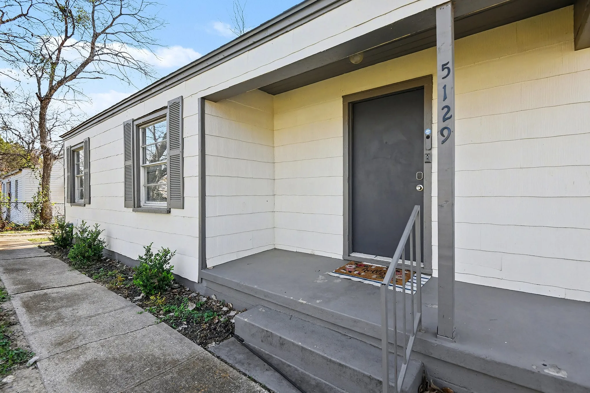 Siding exterior with a covered porch, featuring a dark entry door, an entry railing, and two windows with shutters