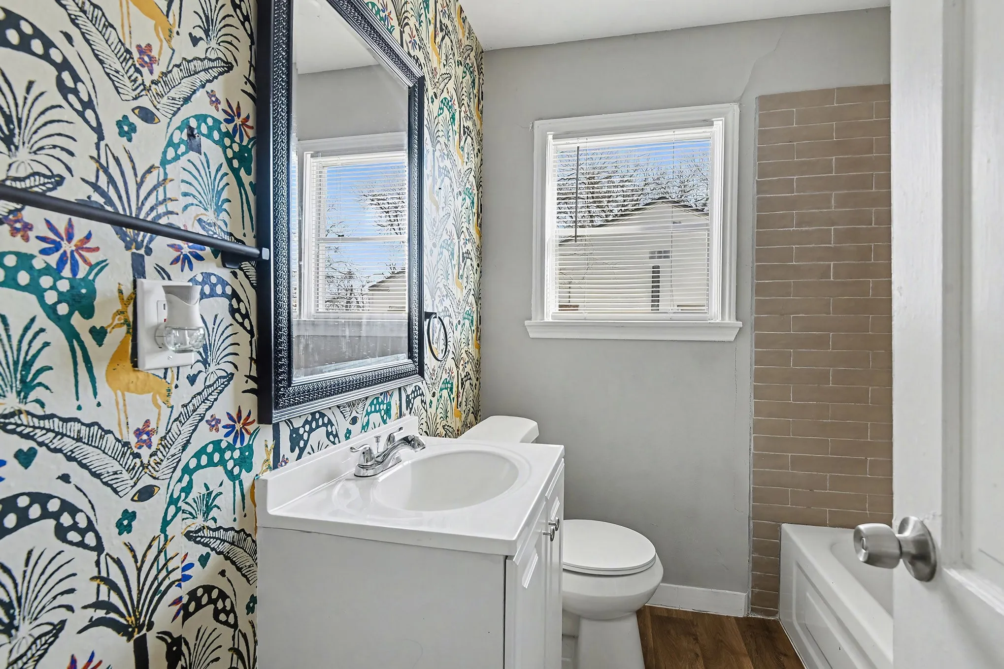 White vanity with an integrated sink, decorative framed mirror, and a window with blinds