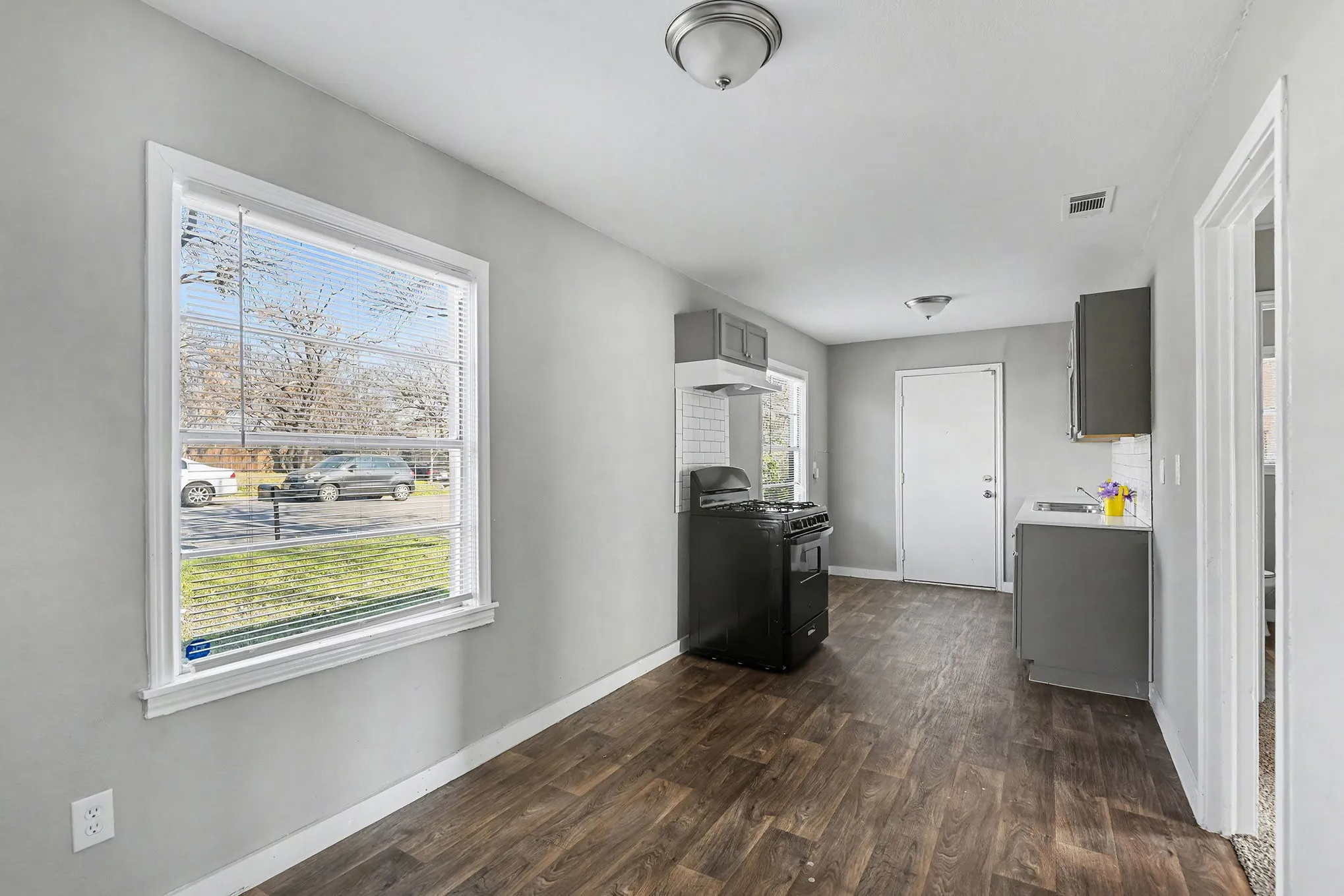 Wood-finish flooring, white subway tile backsplash, white window trim, black range, and gray cabinetry