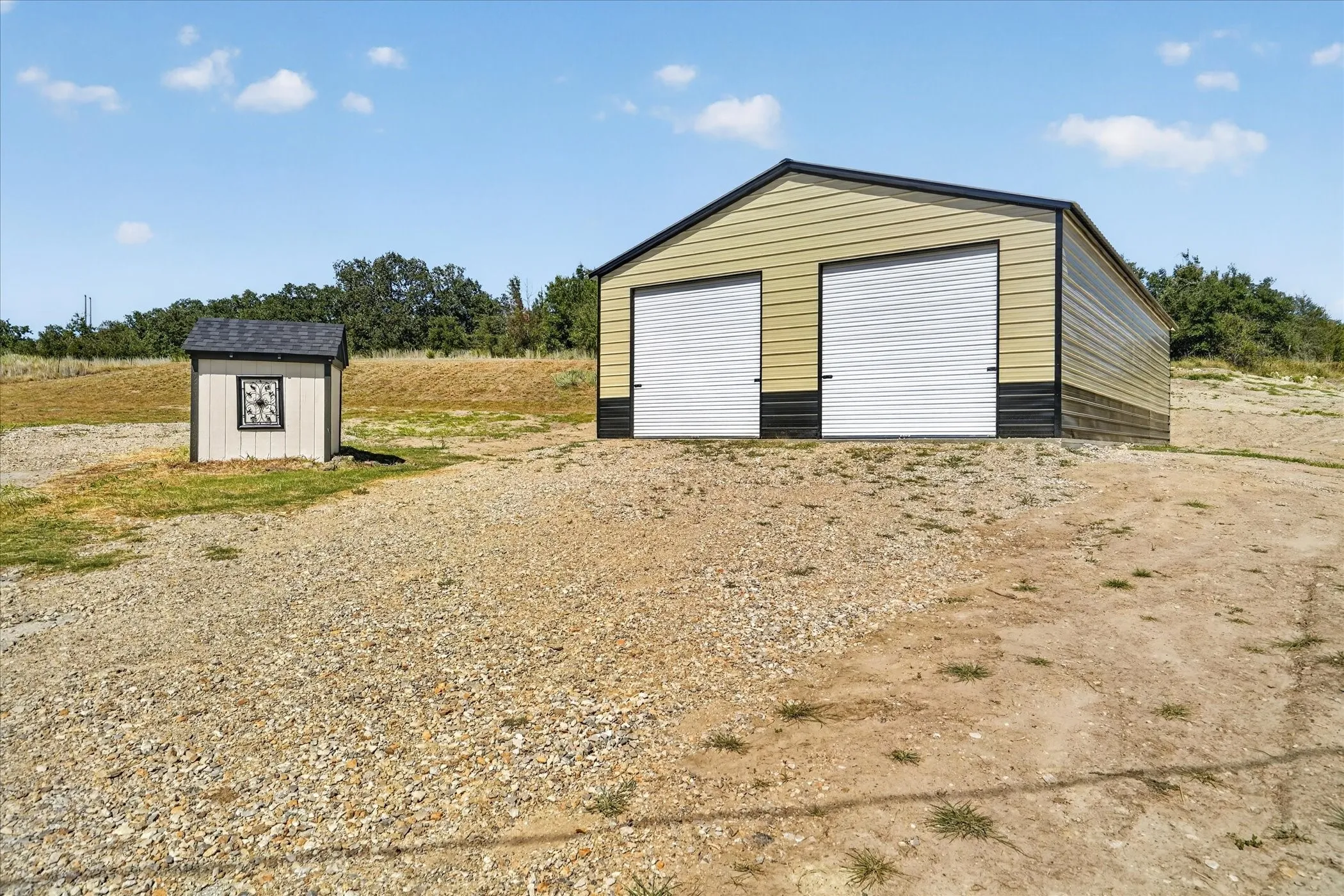 Metal outbuilding with two roll-up doors, accompanied by a small utility shed