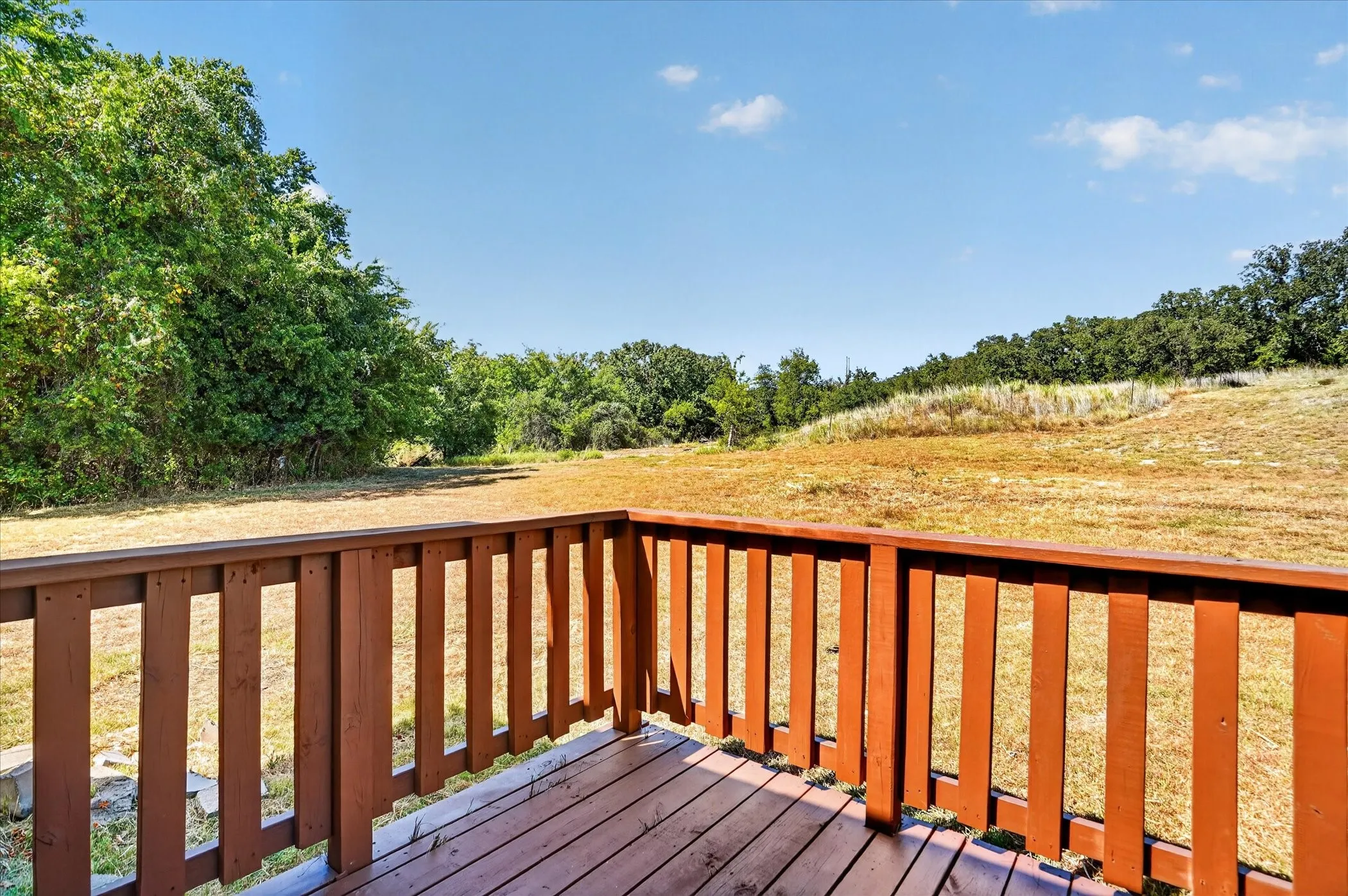 Expansive outdoor deck with wood railing, overlooking an open field and mature trees