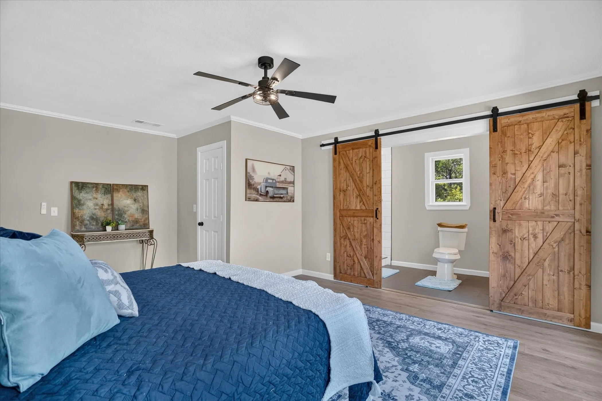 Wood-finish flooring, ceiling fan, crown molding, and two barn doors