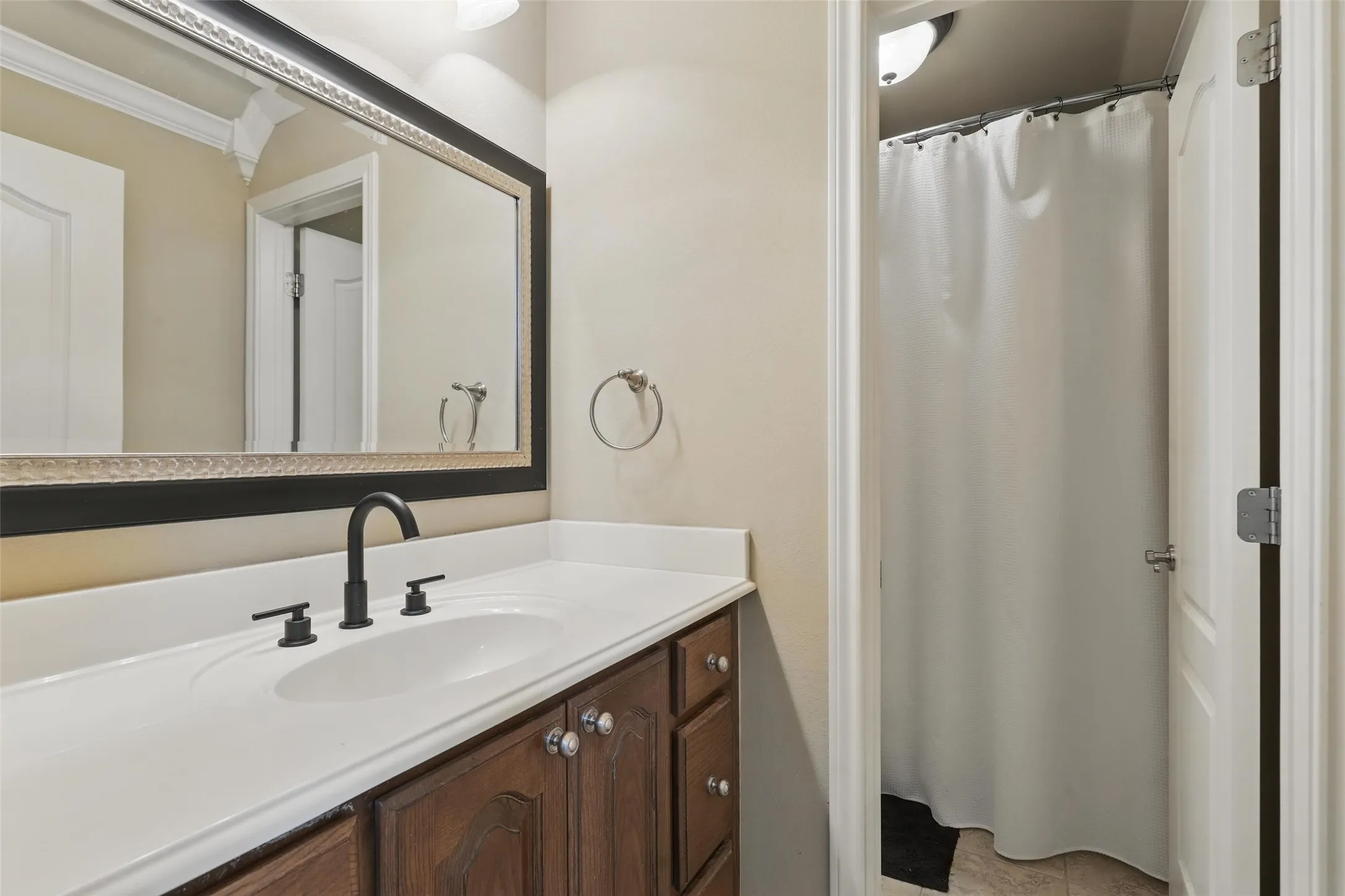 Vanity featuring a white countertop with an integrated sink, dark wood-finish cabinetry, and matte black fixtures