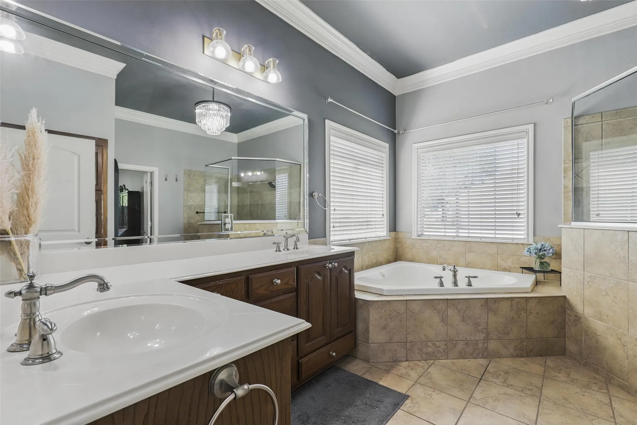 Bathroom featuring a corner soaking tub, dual vanity with undermount sinks, wood-finish cabinetry, and tiled flooring