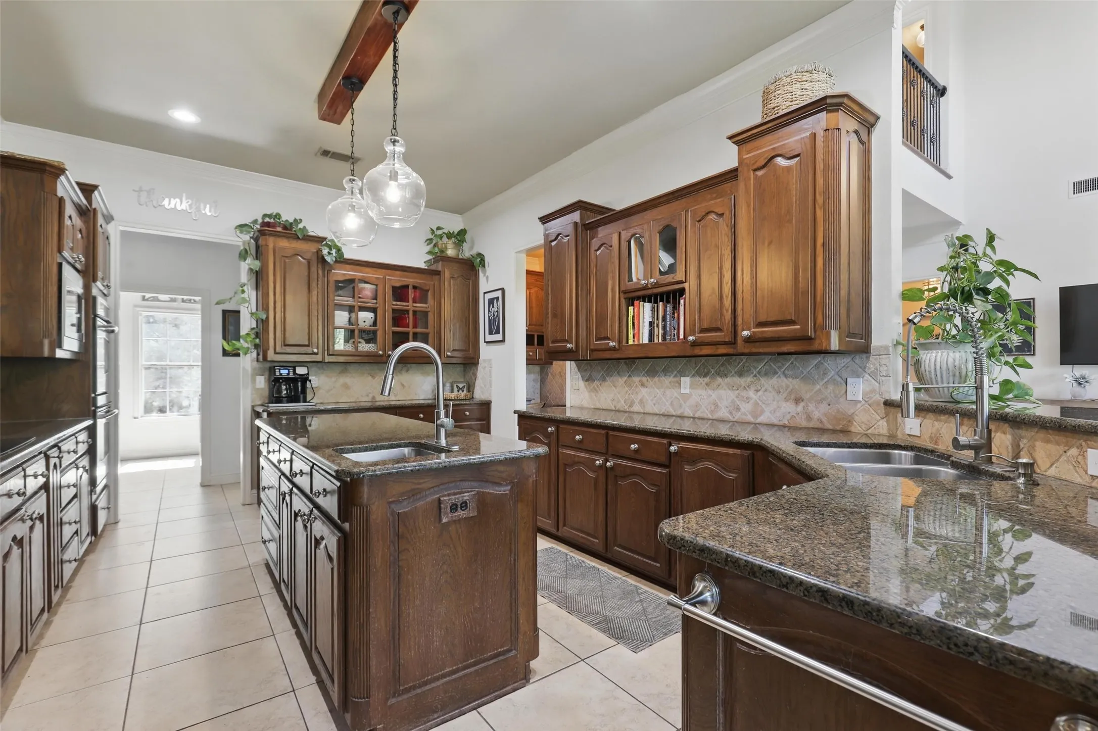 Spacious kitchen featuring an island with an undermount sink, rich wood cabinetry, stone countertops, a tiled backsplash, and recessed lighting