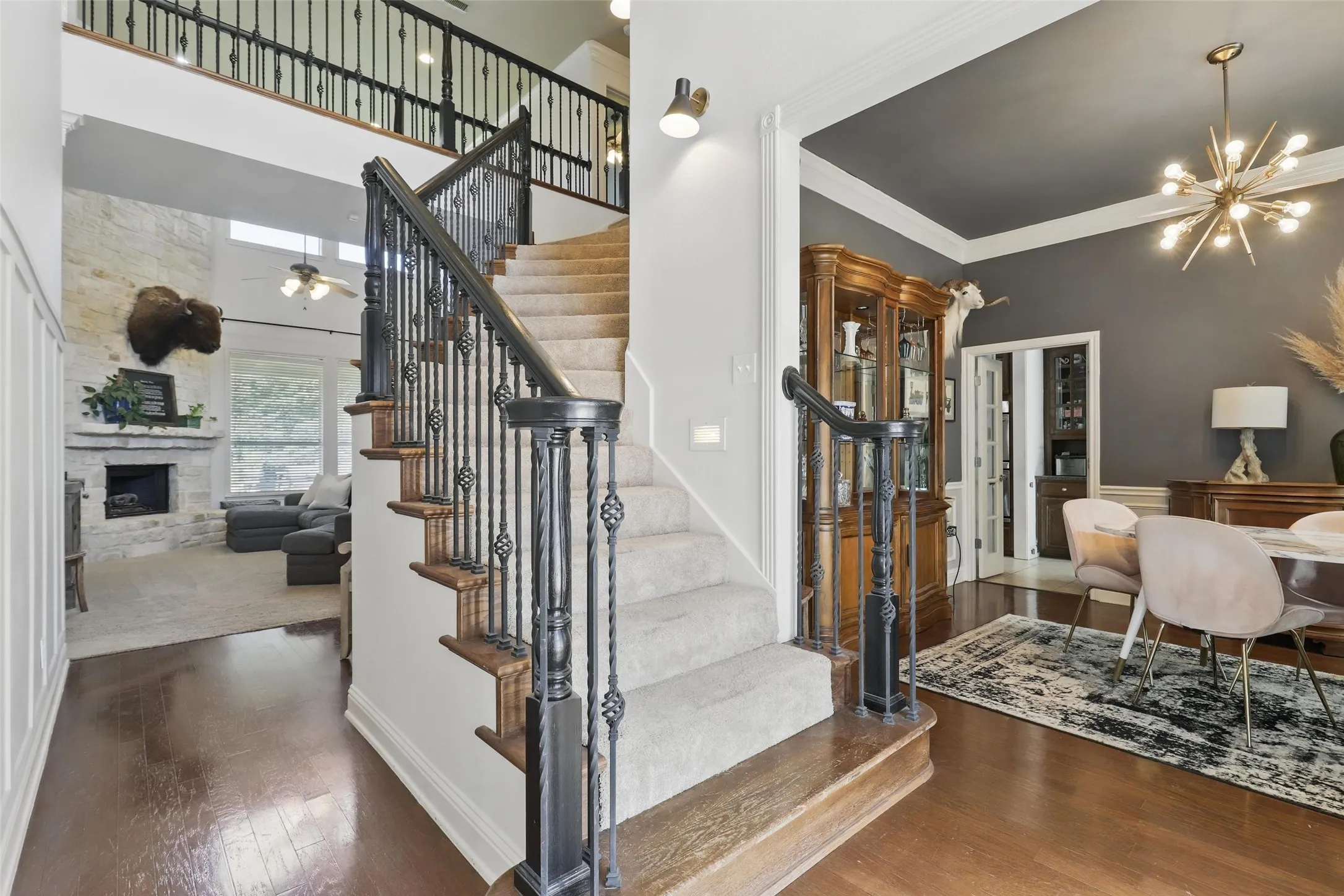 Grand staircase with iron balusters and carpeted treads, complemented by wood-finish flooring