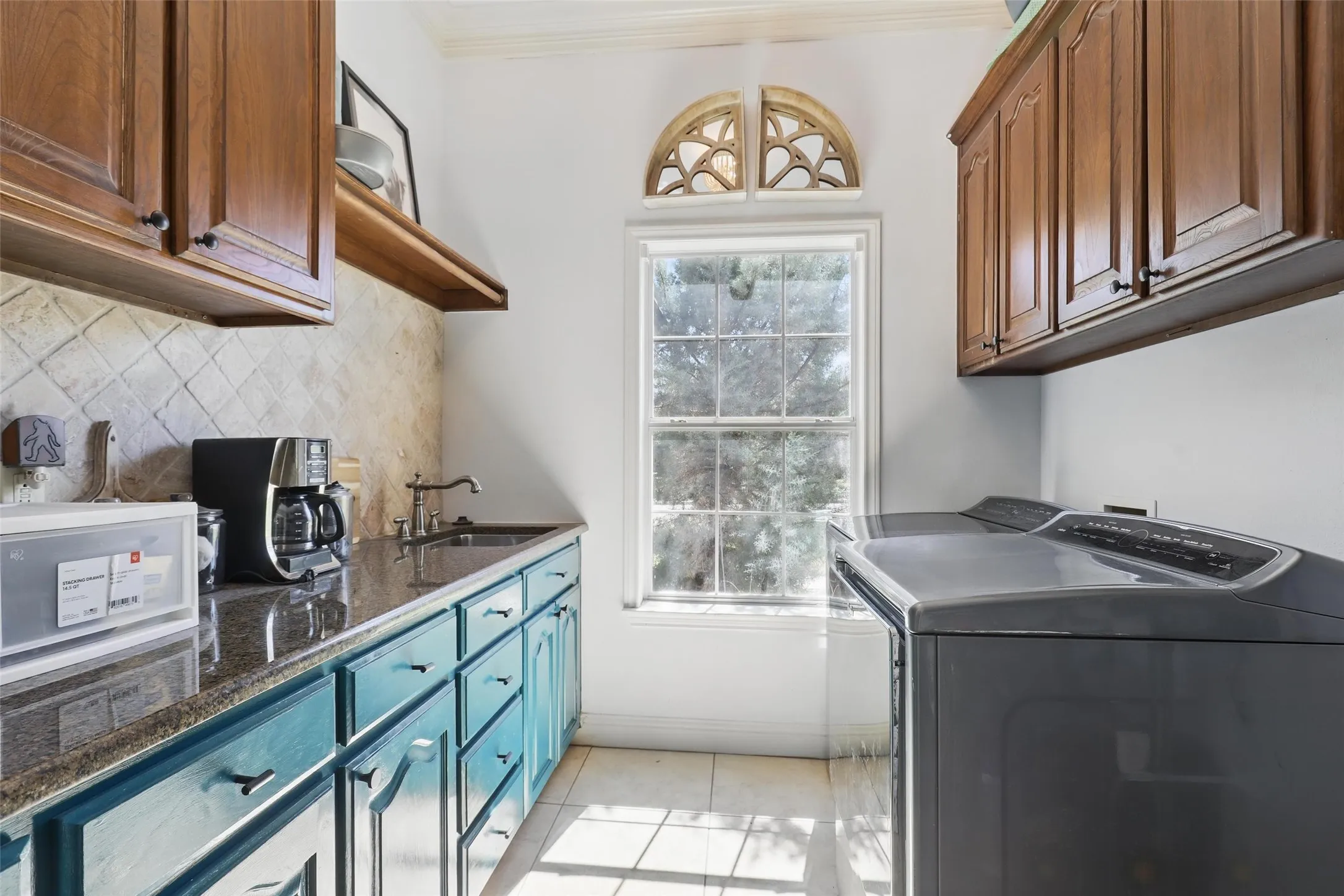 Utility room featuring a built-in sink with a dark countertop, upper wood-finish cabinetry, and lower painted cabinetry with dark hardware