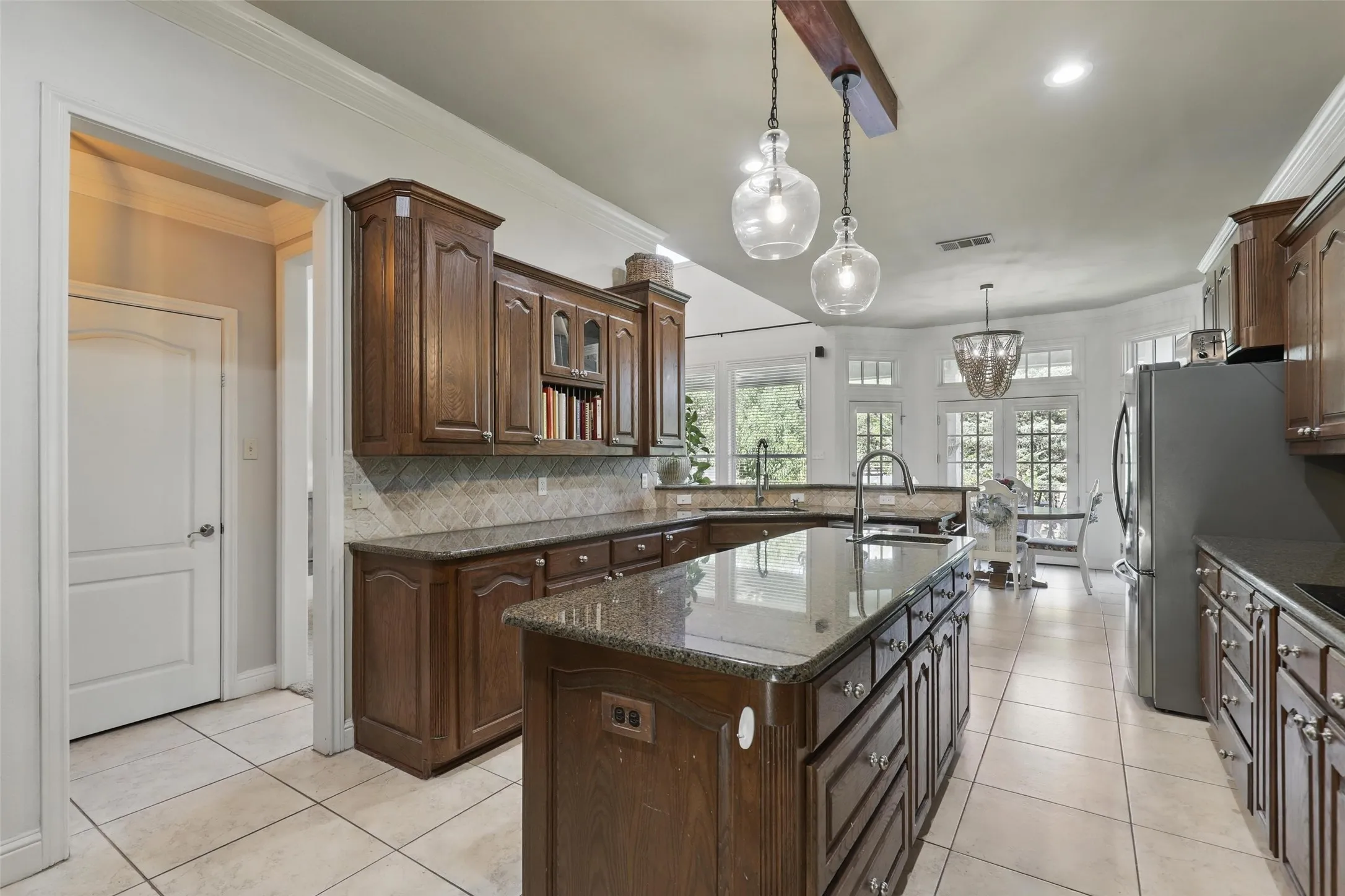 Spacious kitchen featuring a large central island with a sink, extensive dark wood cabinetry, granite countertops, and tile flooring