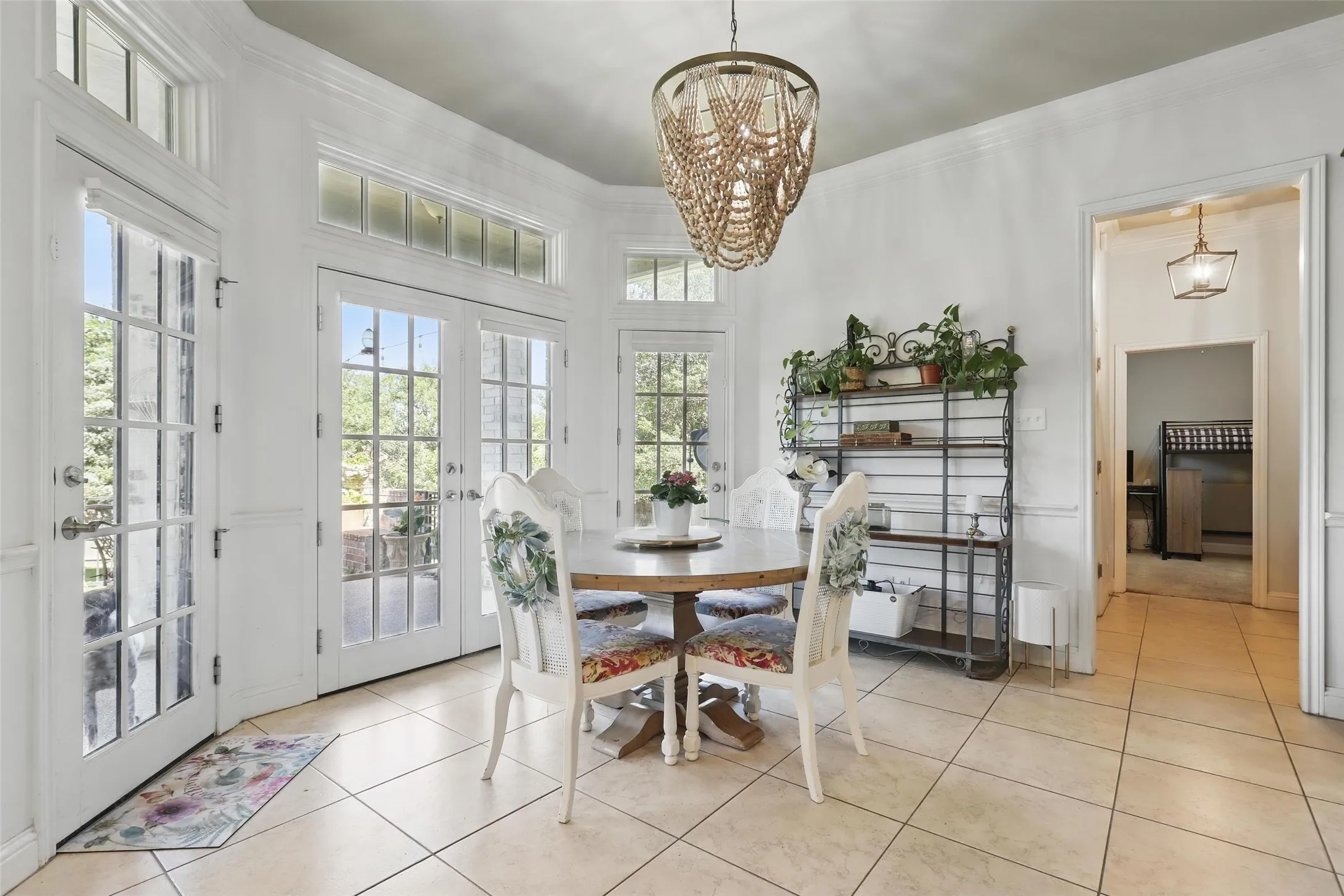 Bright dining area featuring multiple French doors with transom windows, tile flooring, and a unique beaded chandelier