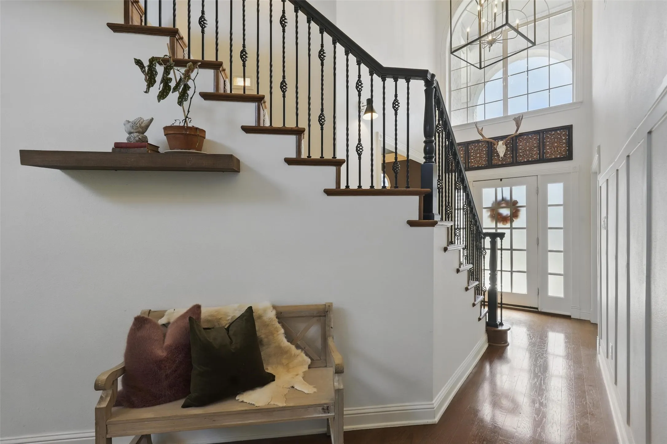Grand entry featuring hardwood flooring, an elegant staircase with wrought iron balusters, high ceilings, and a tall arched window with grid detailing