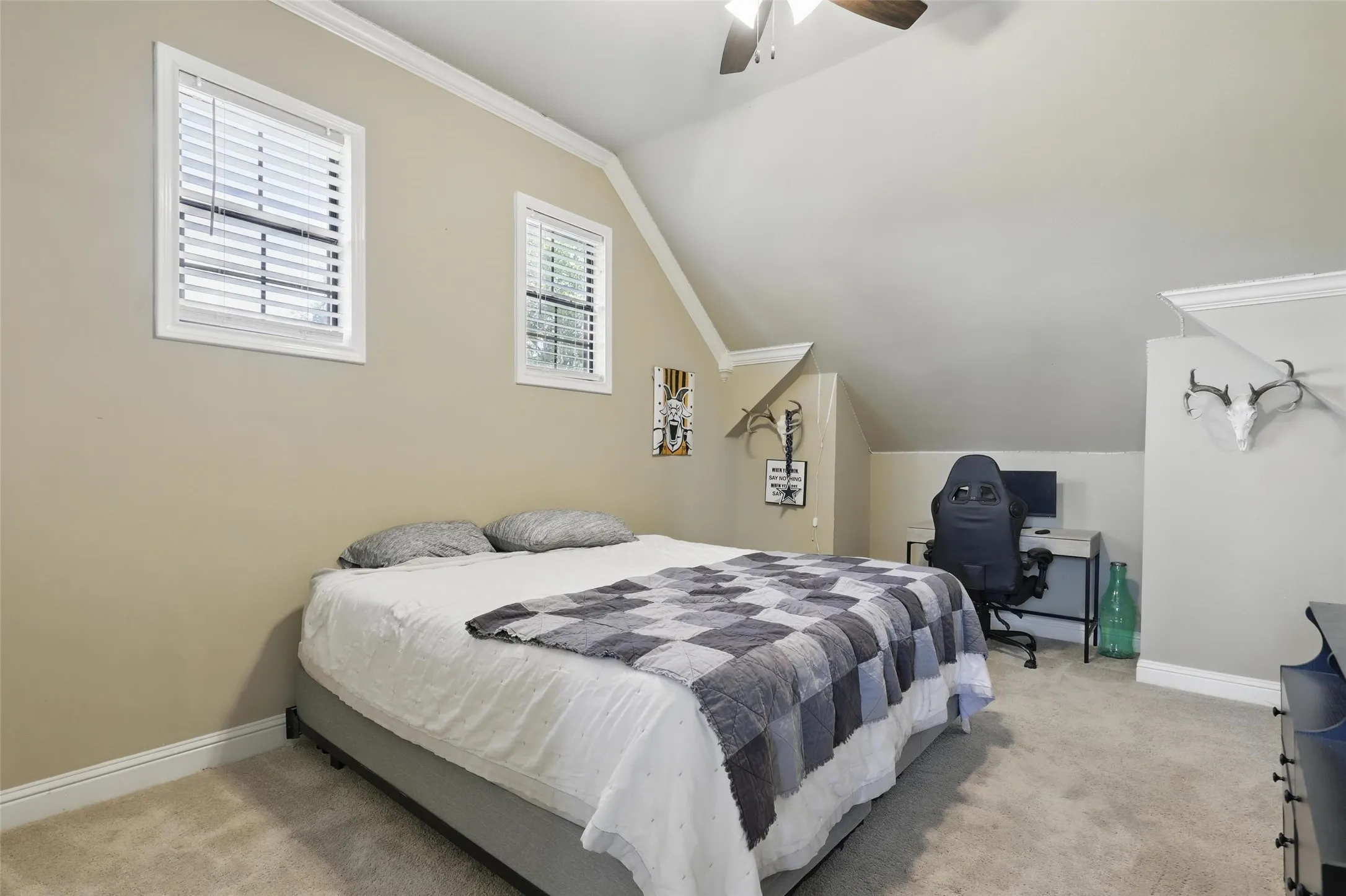 Carpeted bedroom featuring two windows with blinds, a sloped ceiling, crown molding, and a ceiling fan with light fixture