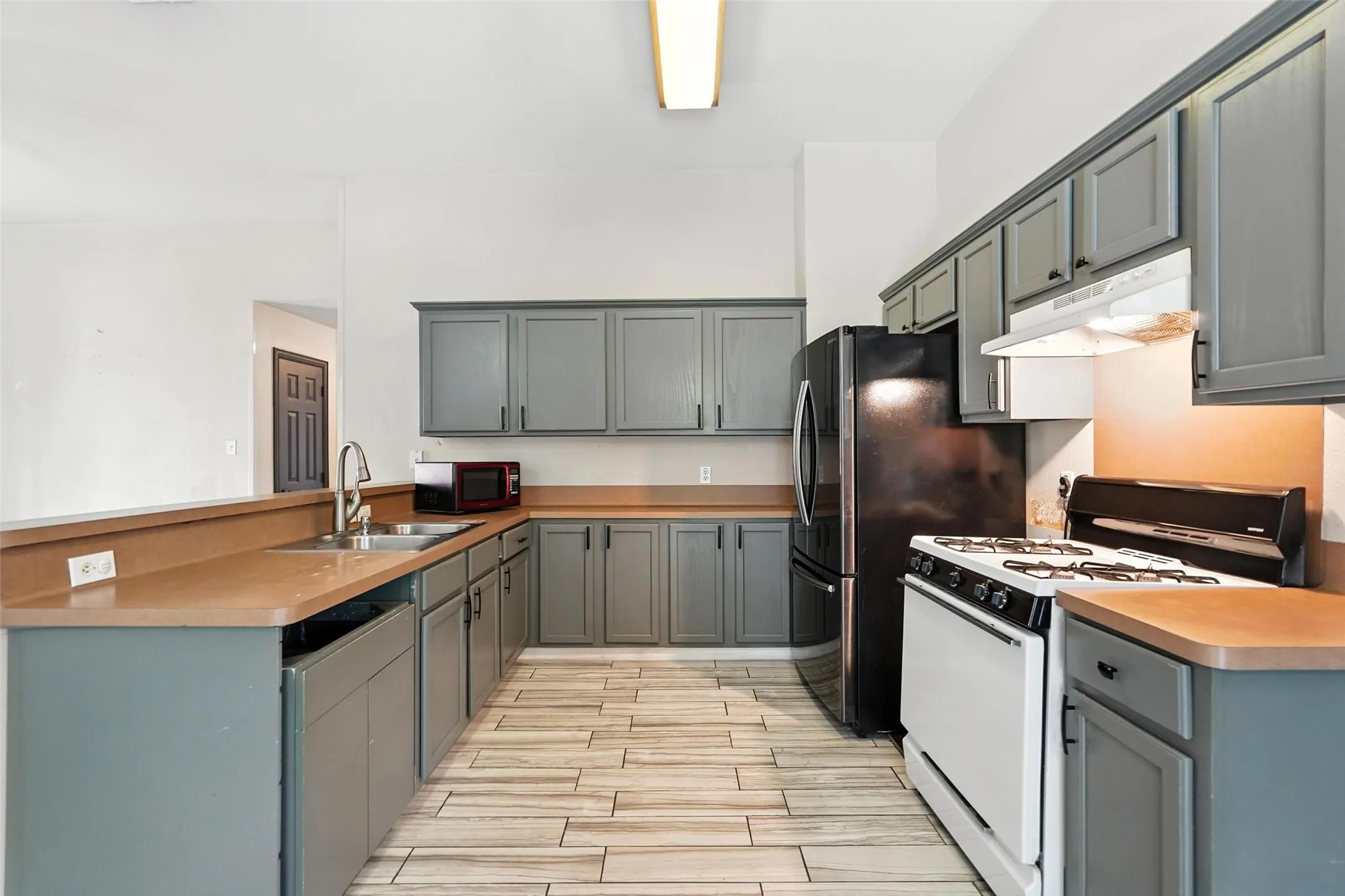 Kitchen with white range with gas cooktop, a peninsula, under cabinet range hood, wood tiled floors, and gray cabinetry