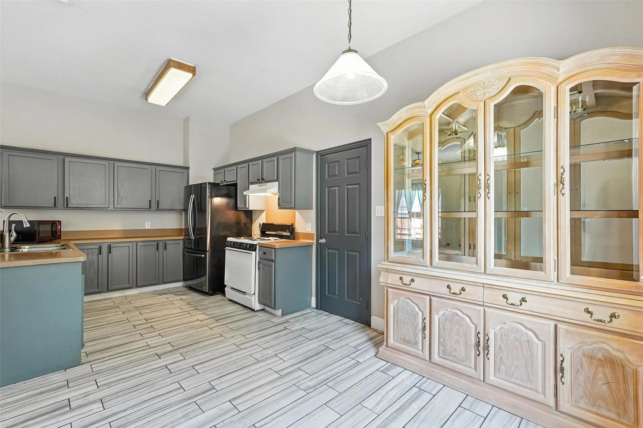 Kitchen featuring white range with gas stovetop, wood tiled floors, gray cabinets, pendant lighting, and under cabinet range hood