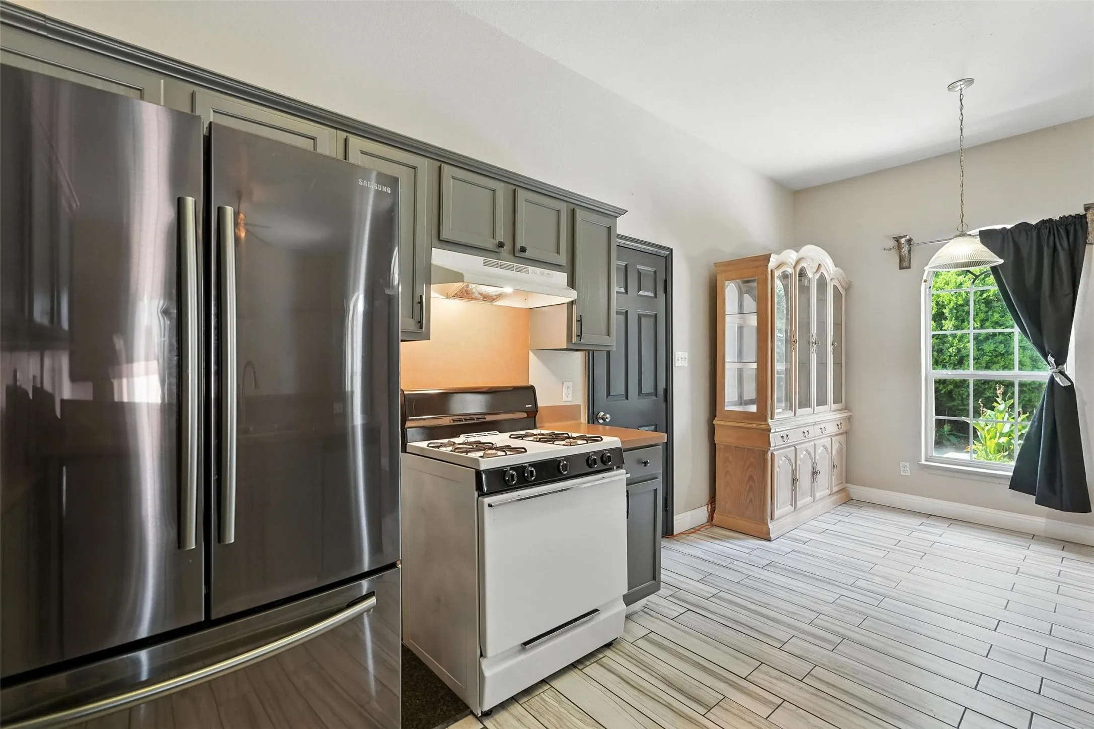 Kitchen with freestanding refrigerator, gas range gas stove, under cabinet range hood, wood tiled floors, and decorative light fixtures