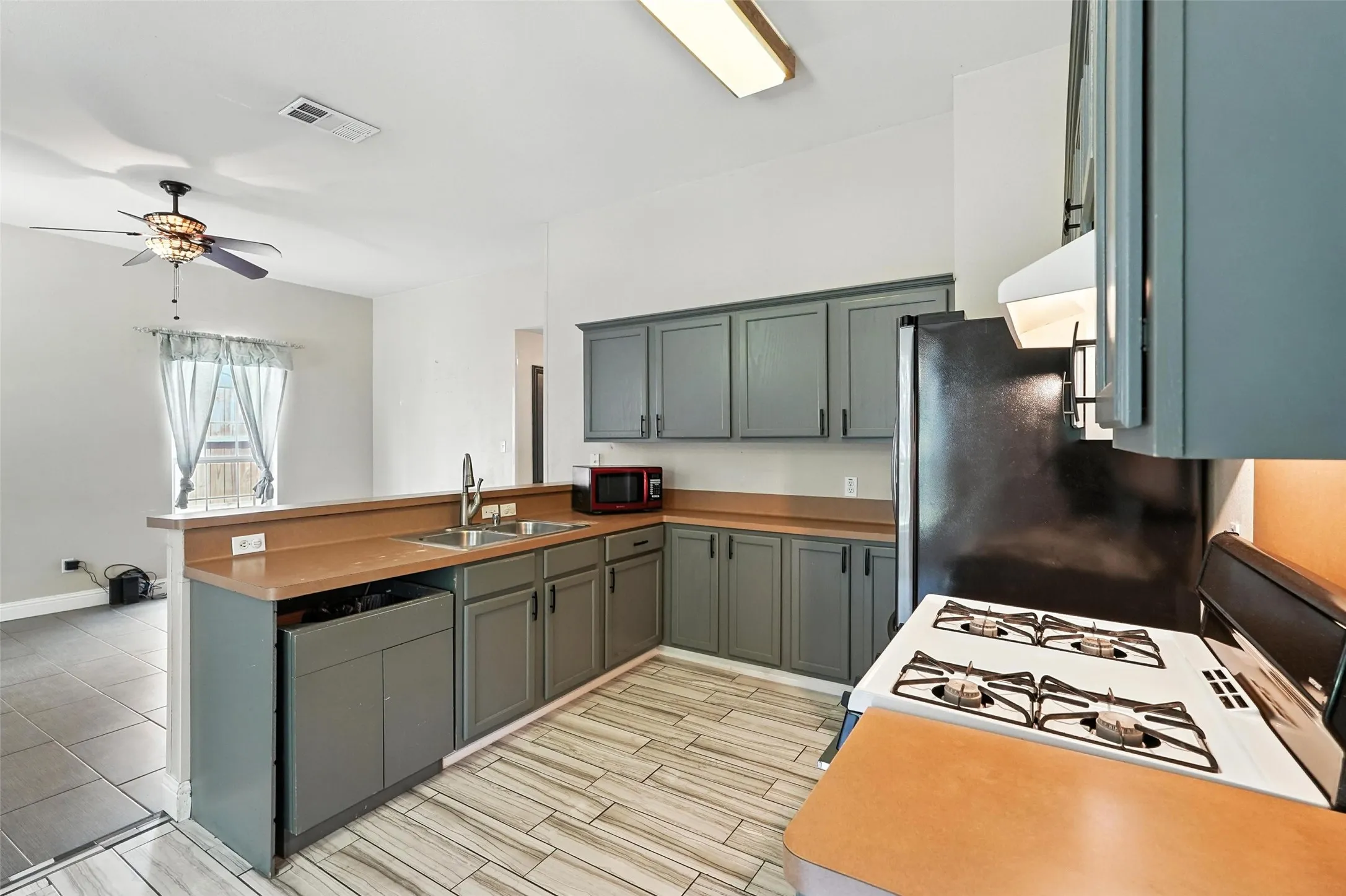 Kitchen with a peninsula, white range with gas stovetop, freestanding refrigerator, wood finish floors, and ceiling fan