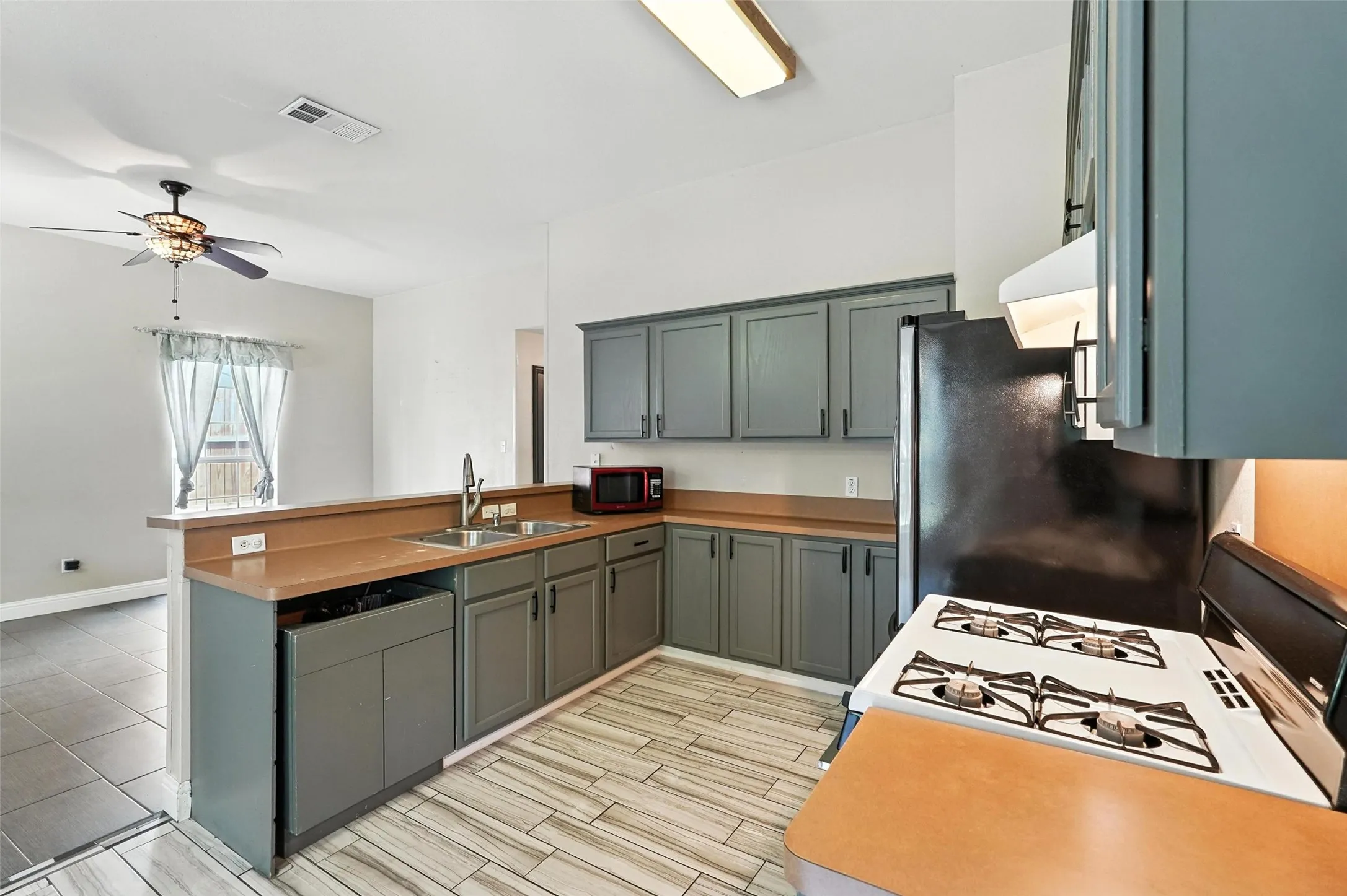 Kitchen with a peninsula, white gas range, freestanding refrigerator, wood finish floors, and a ceiling fan