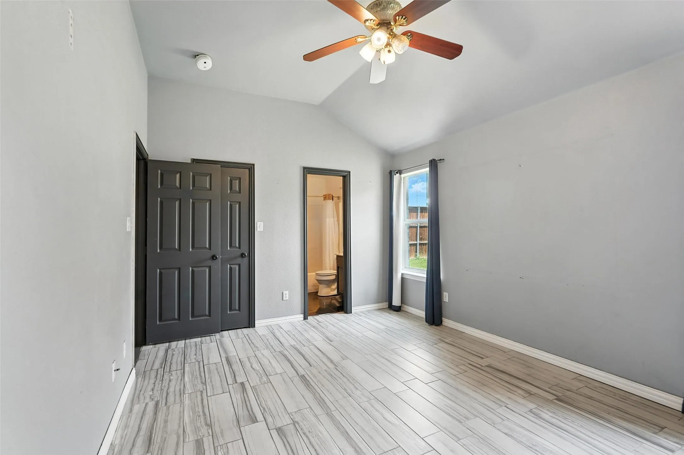 Unfurnished bedroom featuring lofted ceiling, wood tiled floors, a ceiling fan, and connected bathroom