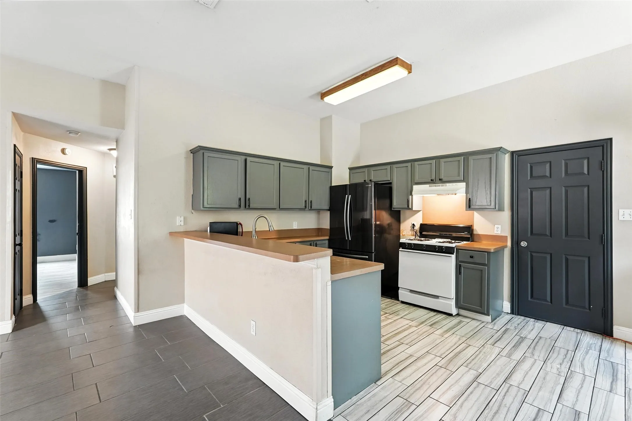 Kitchen with white range with gas cooktop, wood tiled floors, a peninsula, light countertops, and freestanding refrigerator