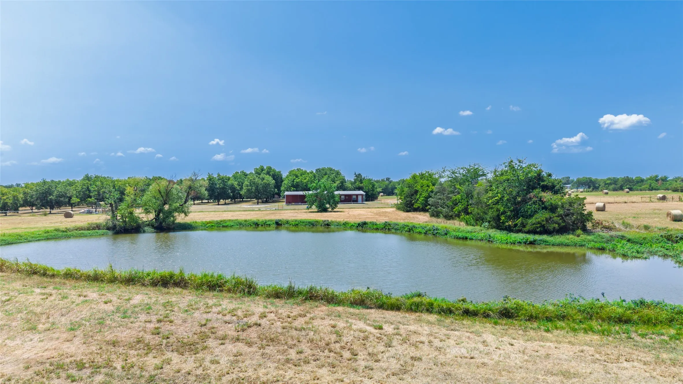 Expansive property featuring a tranquil pond, mature trees, and a distant outbuilding