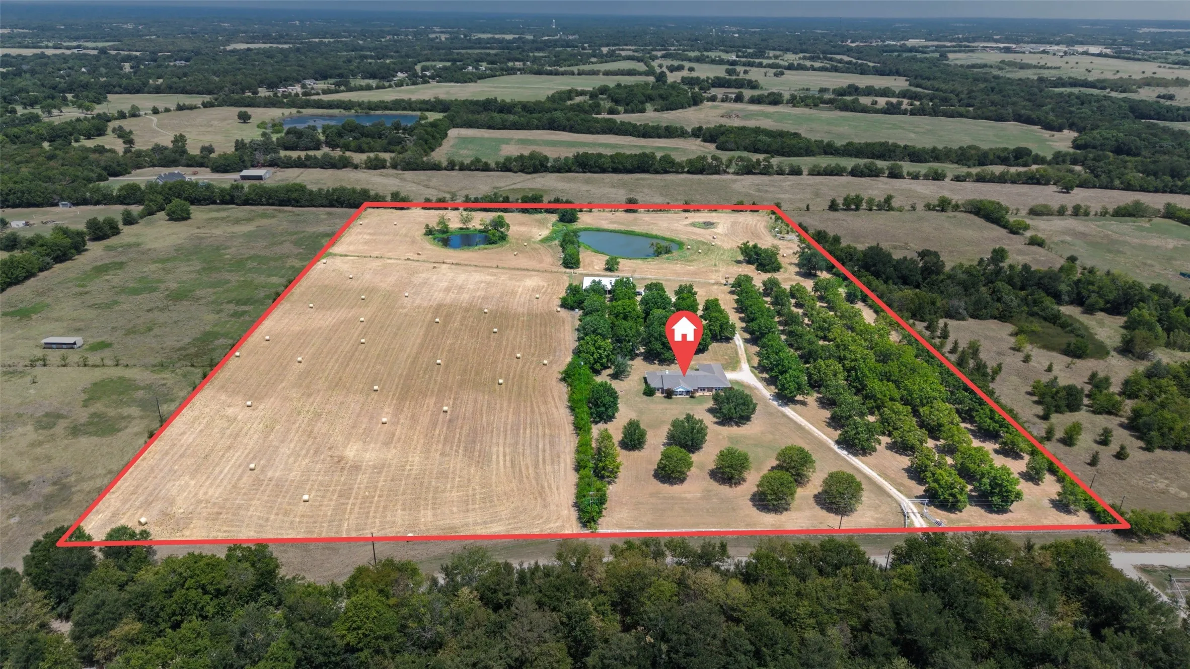 Expansive acreage featuring a single-story residence, multiple ponds, mature trees, and open fields with hay bales