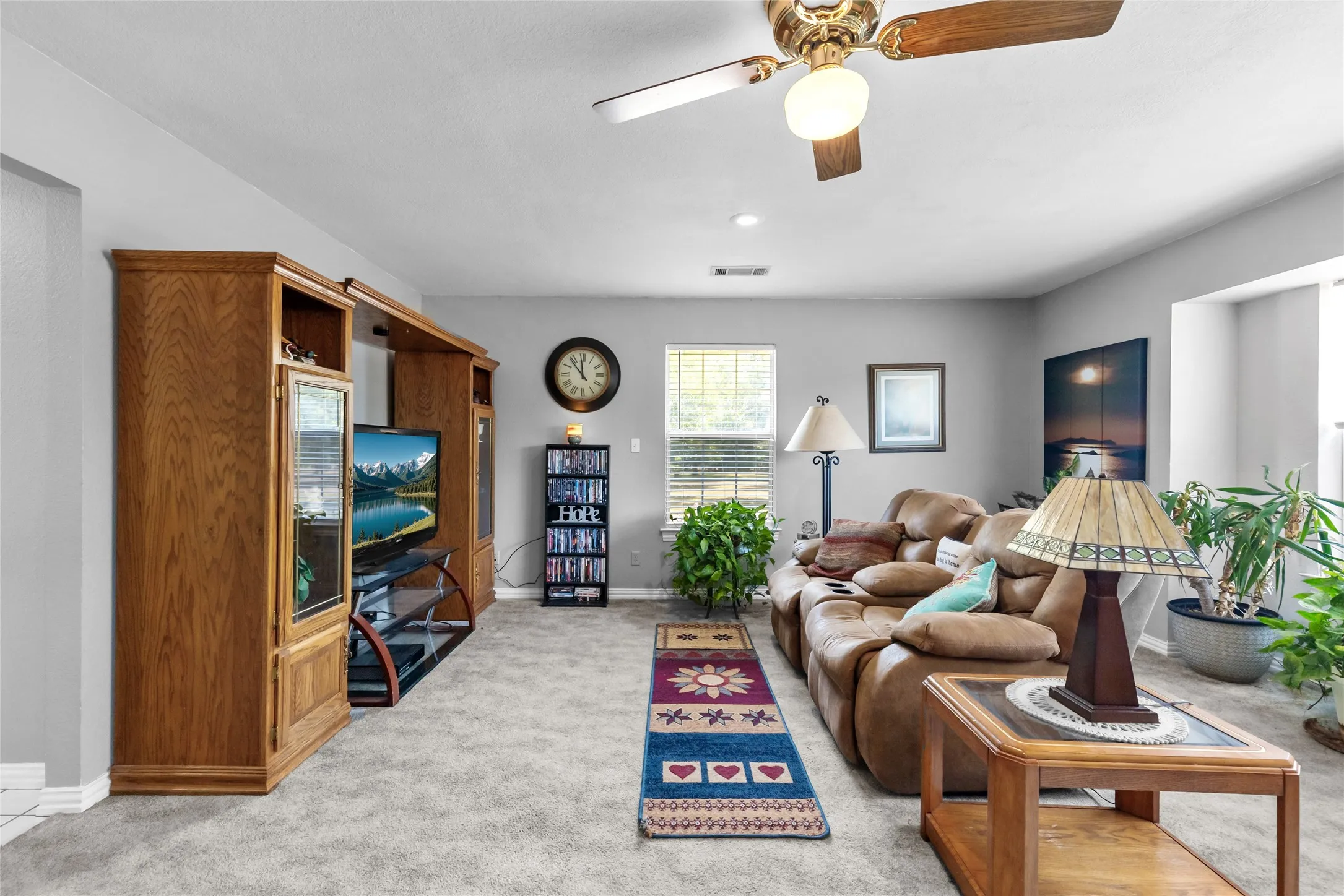 Carpeted living area featuring a ceiling fan with integrated lighting and built-in wood-finish media cabinetry