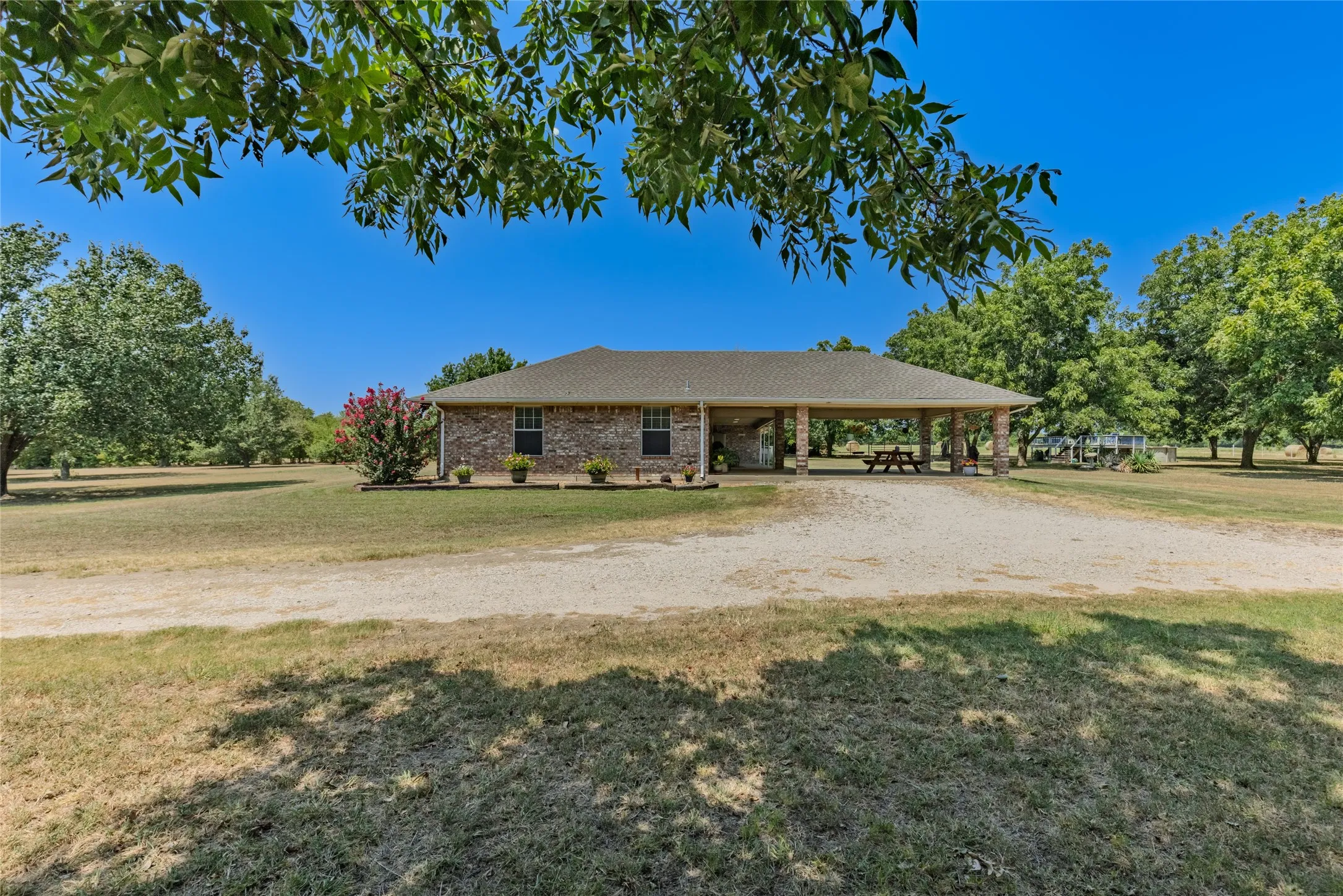 Brick exterior, expansive gravel driveway, mature trees, covered patio, lush lawn