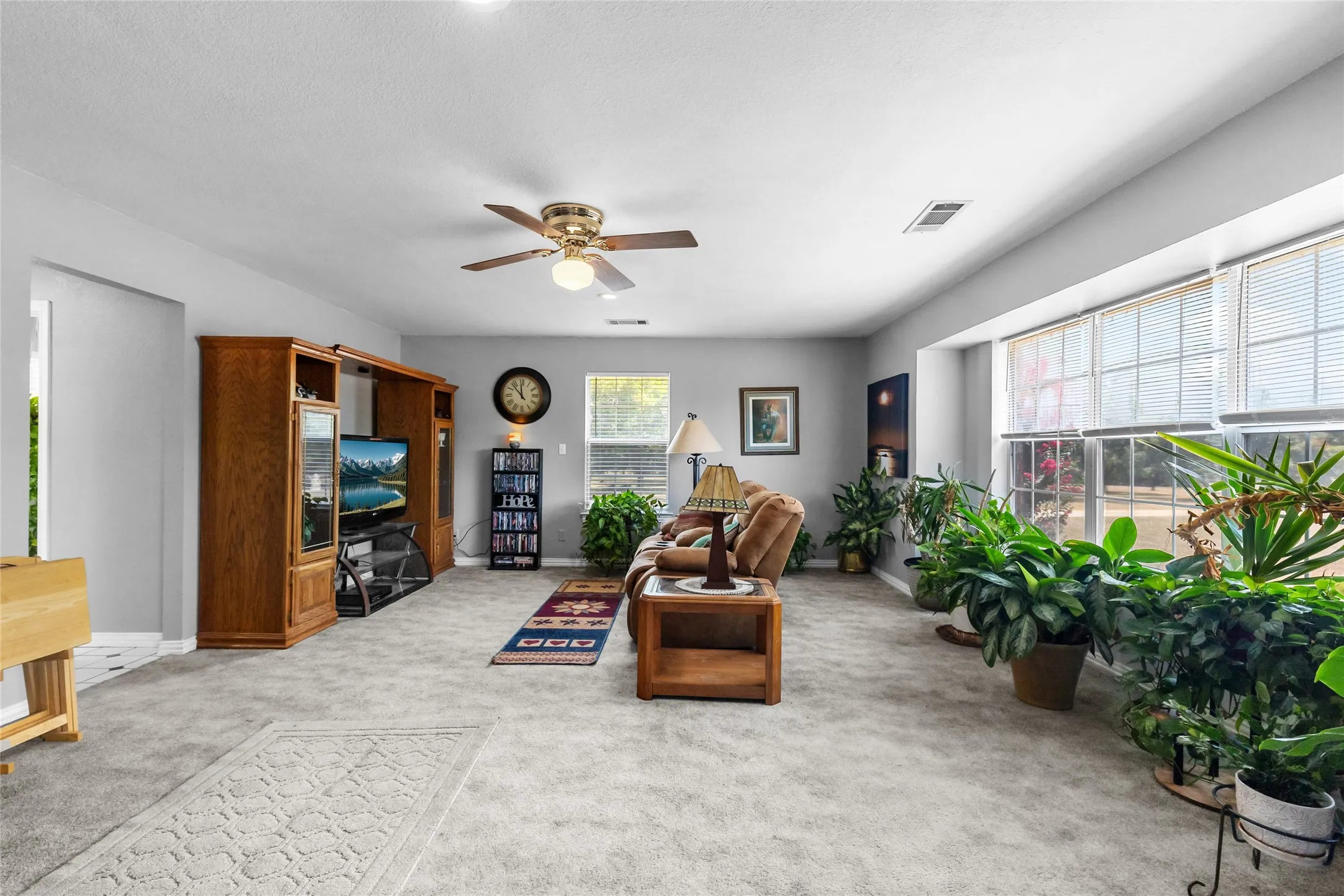 Spacious living area featuring light gray wall paint, light gray carpet, and a large window with white blinds