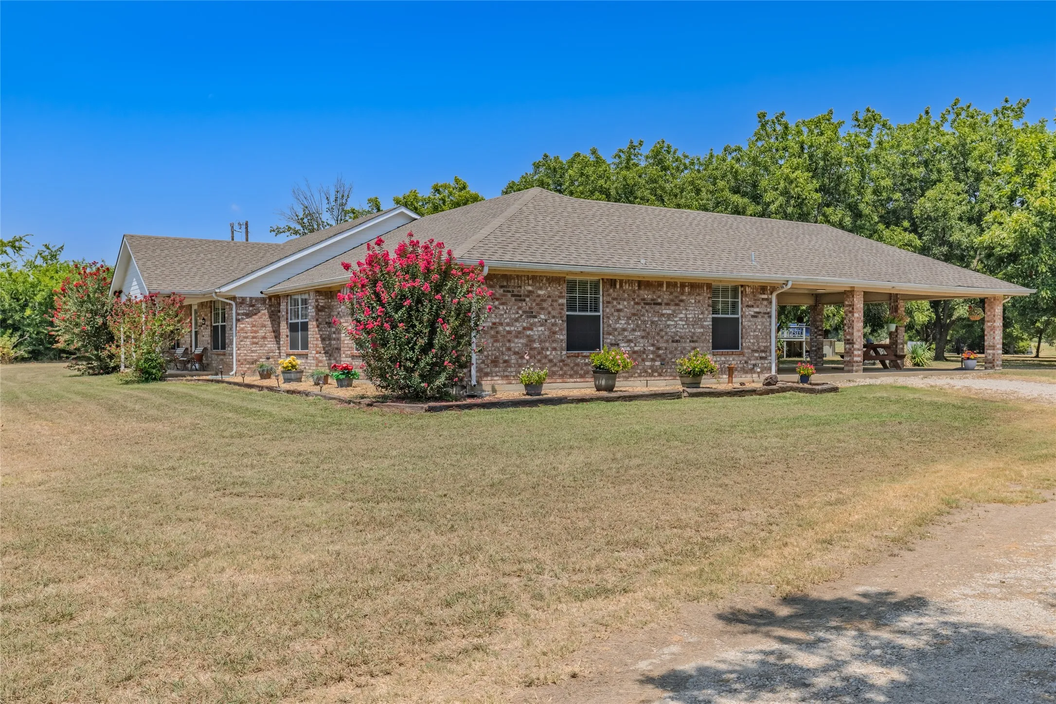 Brick exterior, covered porch, mature trees, landscaped planting beds, and a gravel driveway