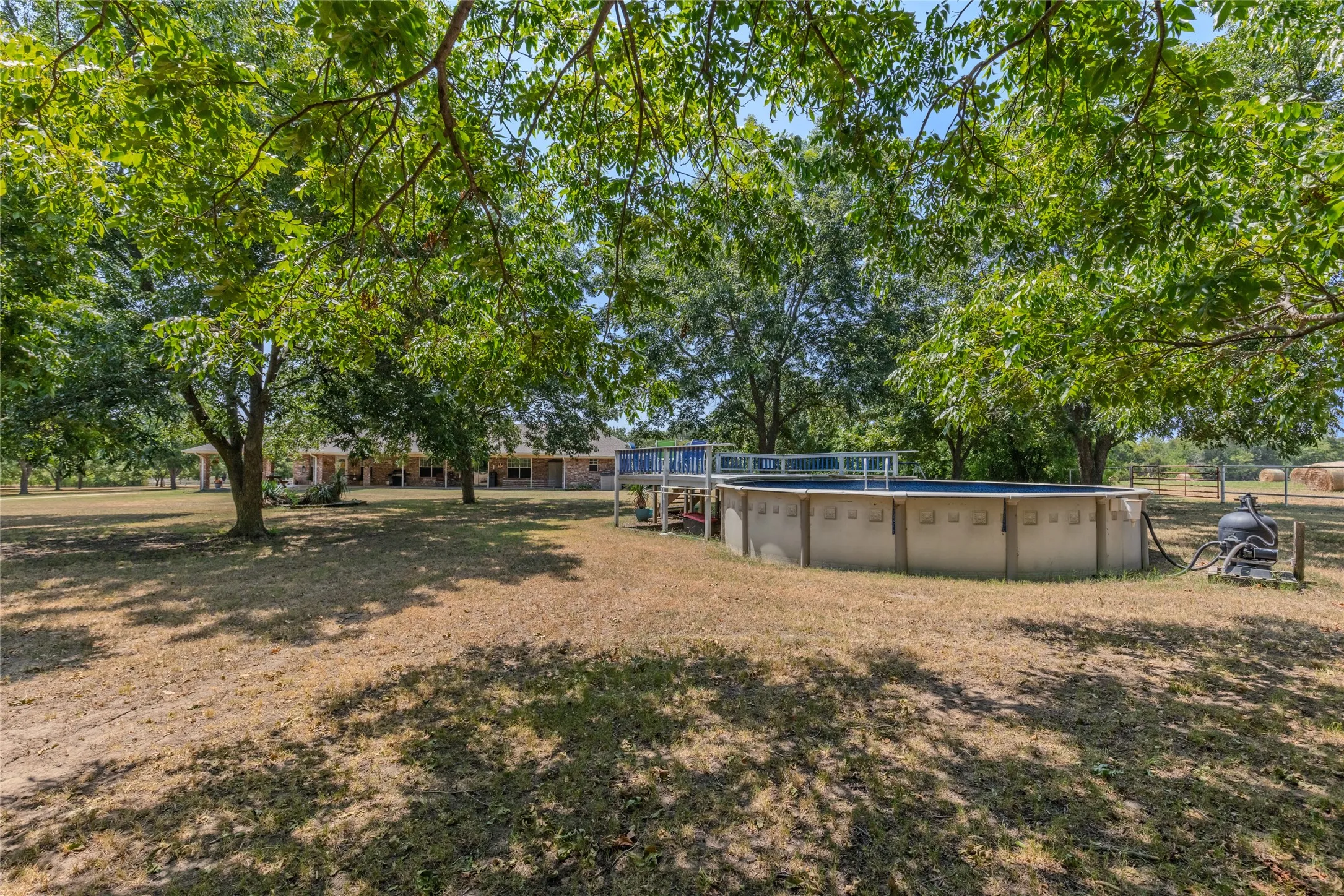 Expansive yard with mature trees providing shade, featuring an above-ground pool with a surrounding deck