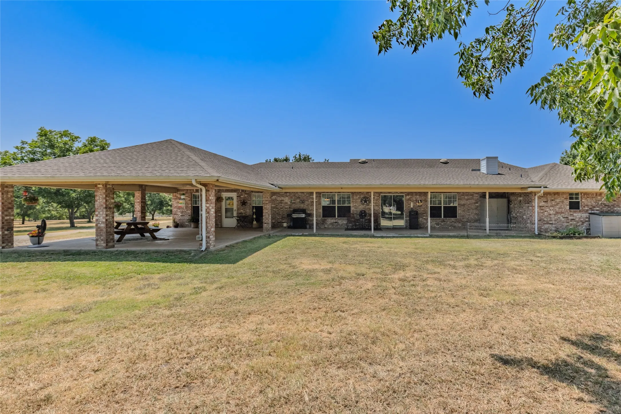 Extensive covered patio with brick columns, concrete flooring, and a shingle roof