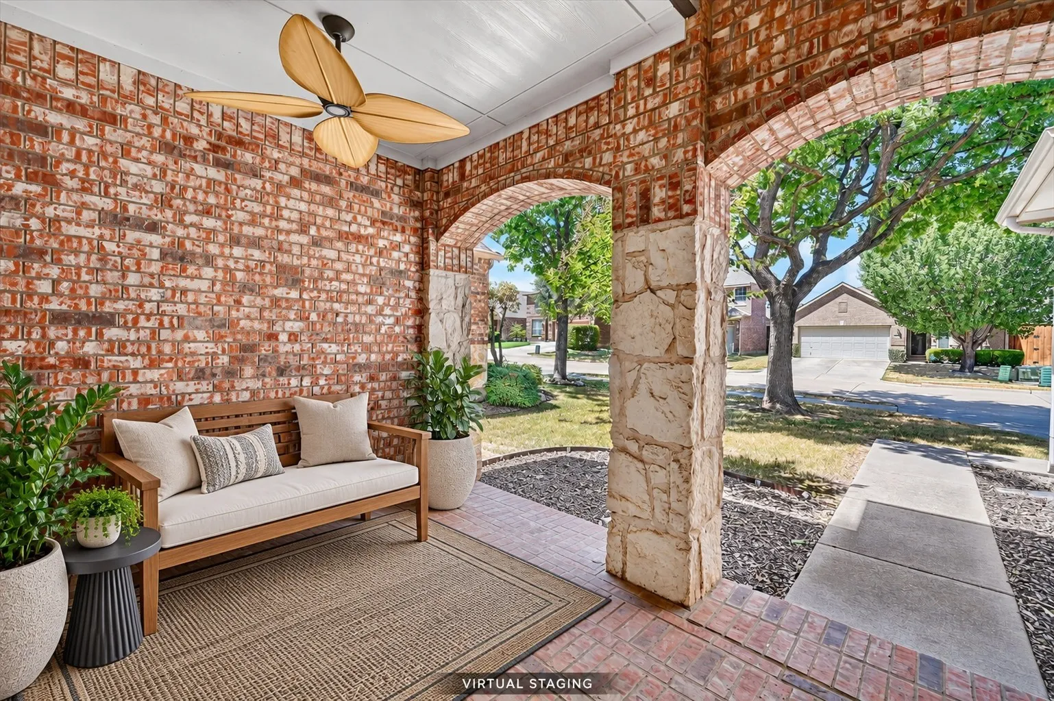 Spacious covered front porch featuring brick and stone columns, brick walls, and an overhead ceiling fan.