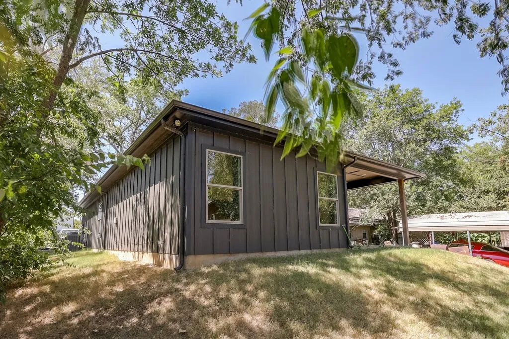 Vertical siding exterior with light-colored window frames and a covered side patio