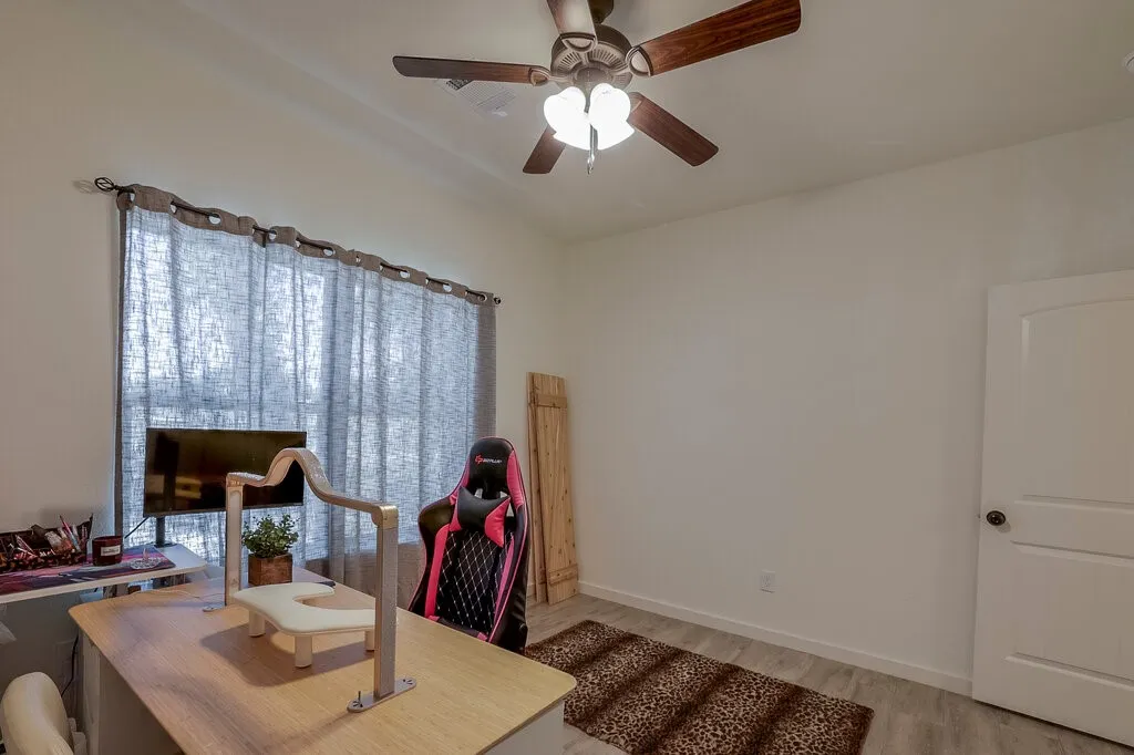 Ceiling fan with light fixture, window with drapes, paneled interior door, and wood-finish flooring